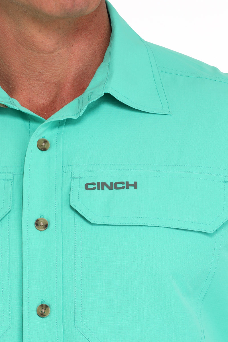 Close-up of a teal shirt with 'CINCH' logo on a white background