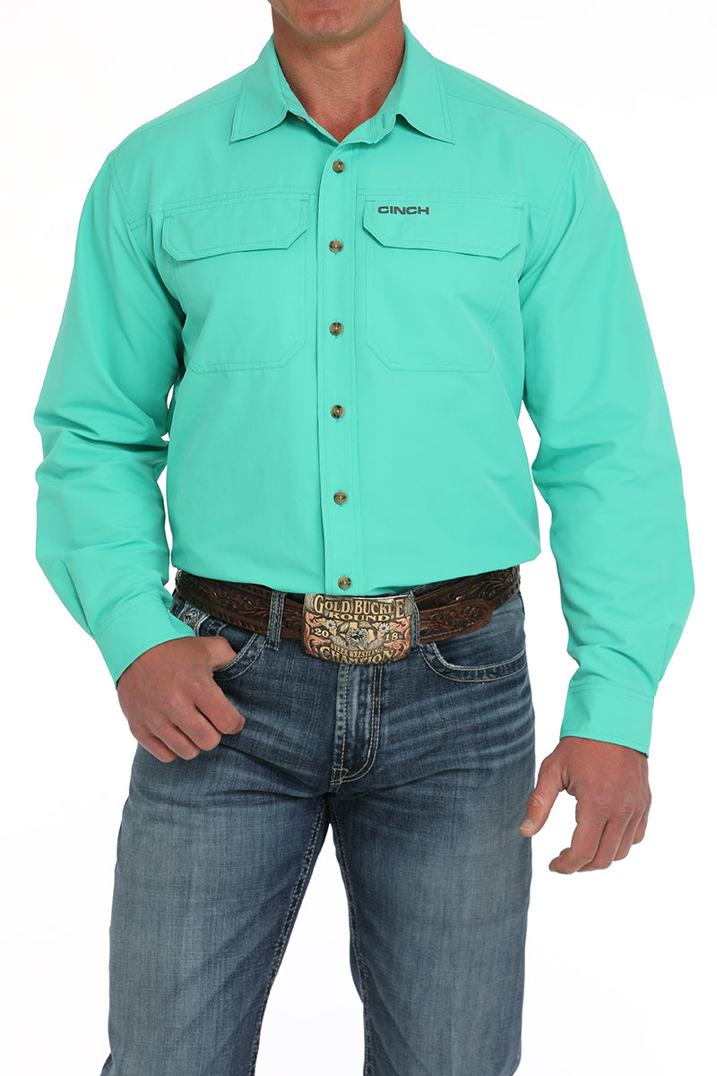 Man wearing a light green shirt and jeans with a belt buckle.