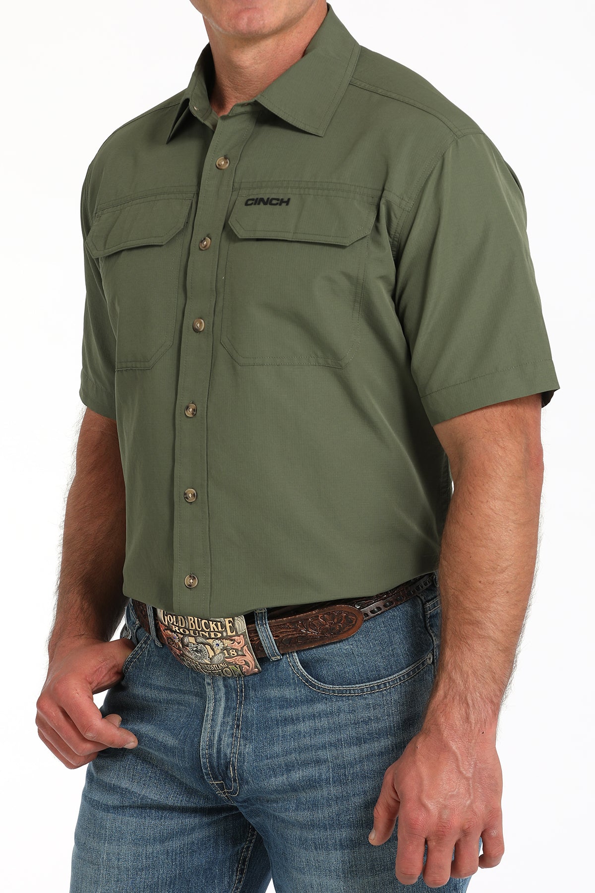Man wearing a green short-sleeve shirt with a brand logo, paired with blue jeans.