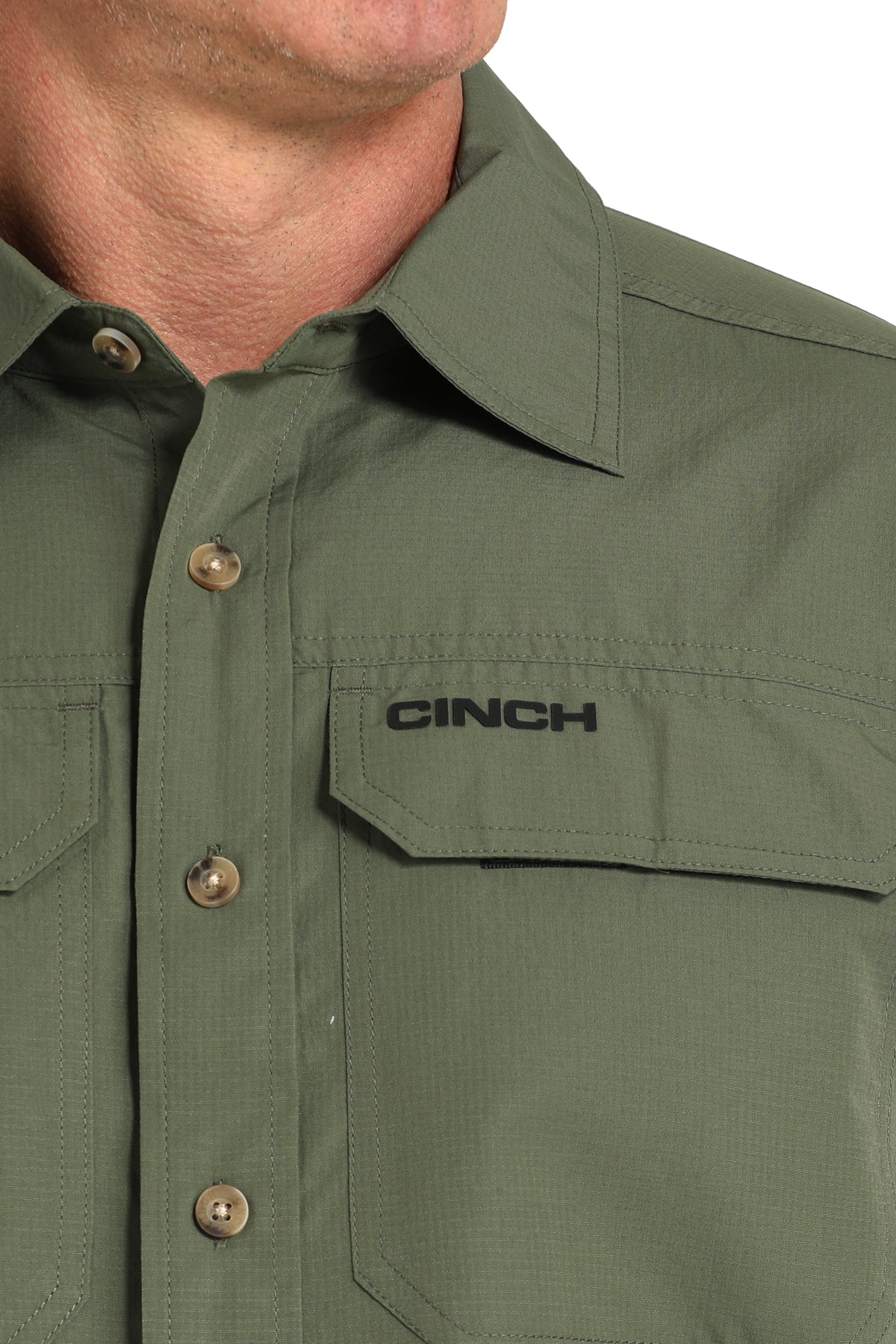Close-up of a green shirt with 'Cinch' branding on a plain background