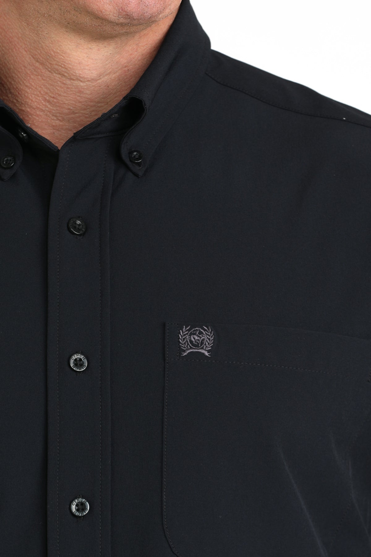 Close-up of a black button-up shirt with a logo on the chest pocket against a white background