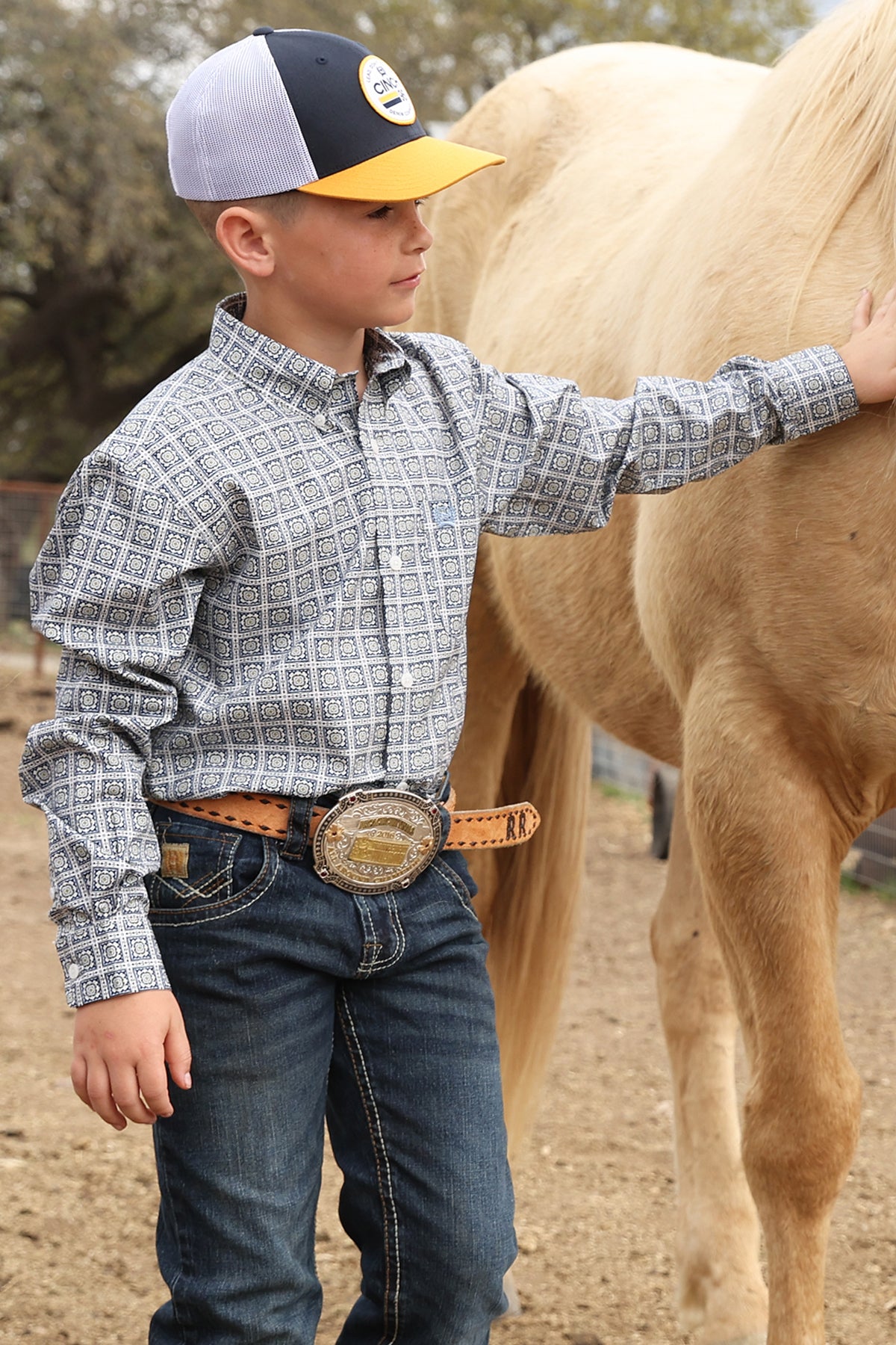 Young boy in cowboy attire standing next to a horse