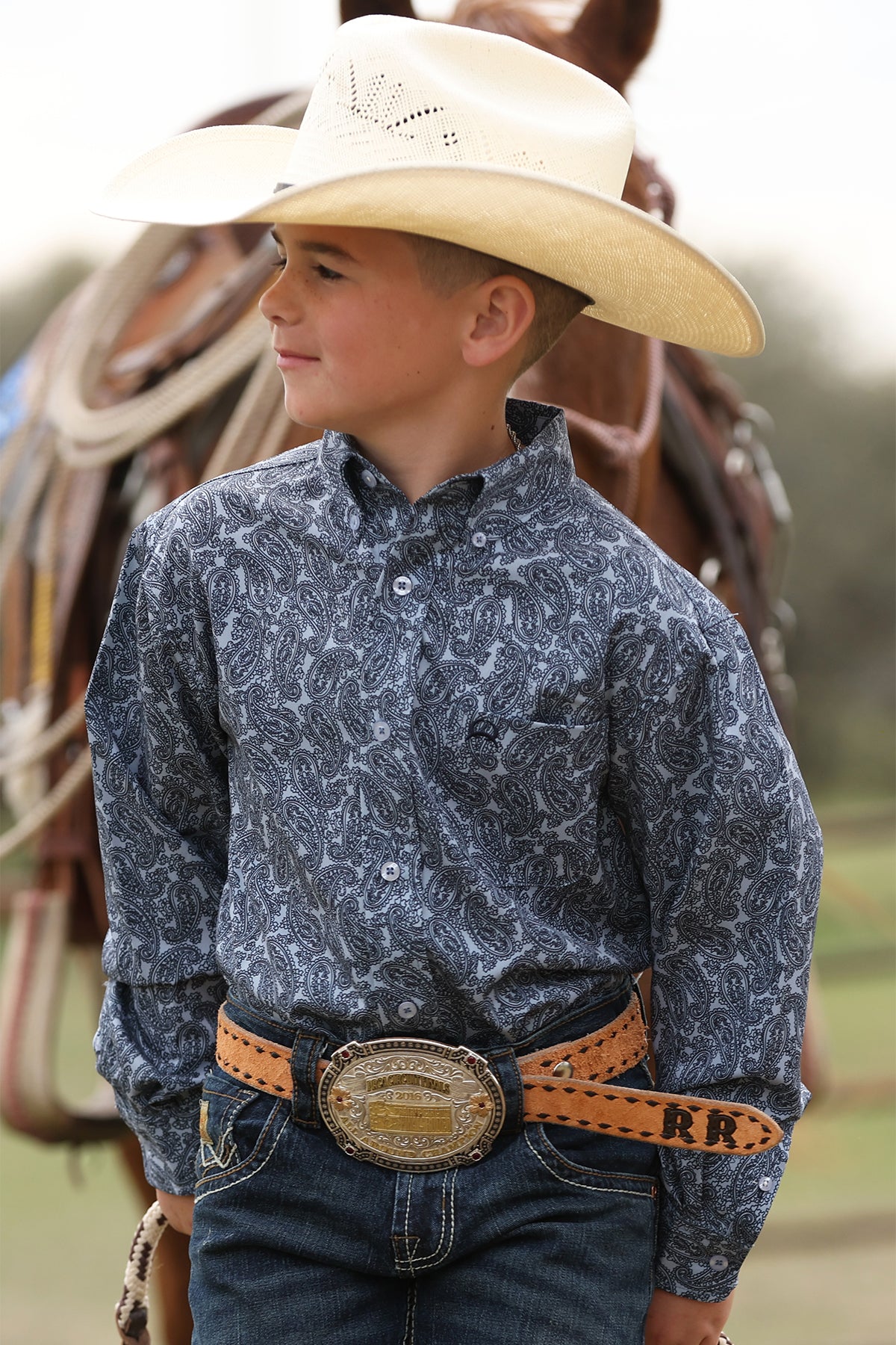 Young boy in a blue print CINCH ARENAFLEX long sleeve shirt with a horse in the background