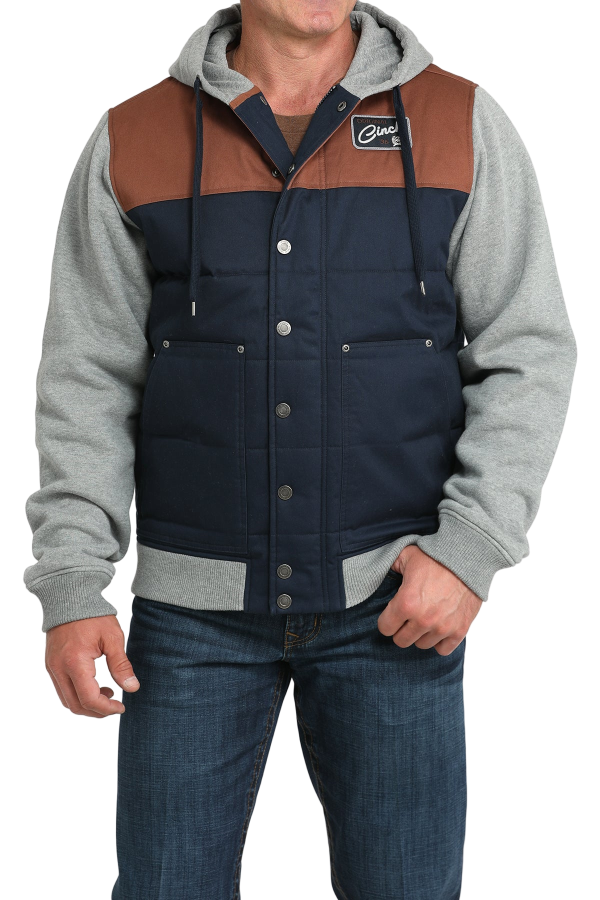 Man wearing a navy and brown snap-front jacket with light gray sleeves and a hood, paired with blue jeans