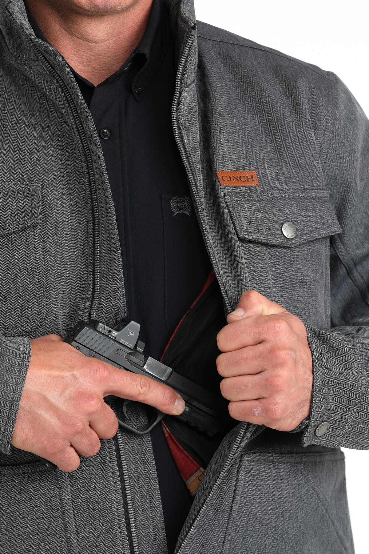 Close-up of a man wearing a gray jacket showing a partial firearm going into the concealed carry pocket