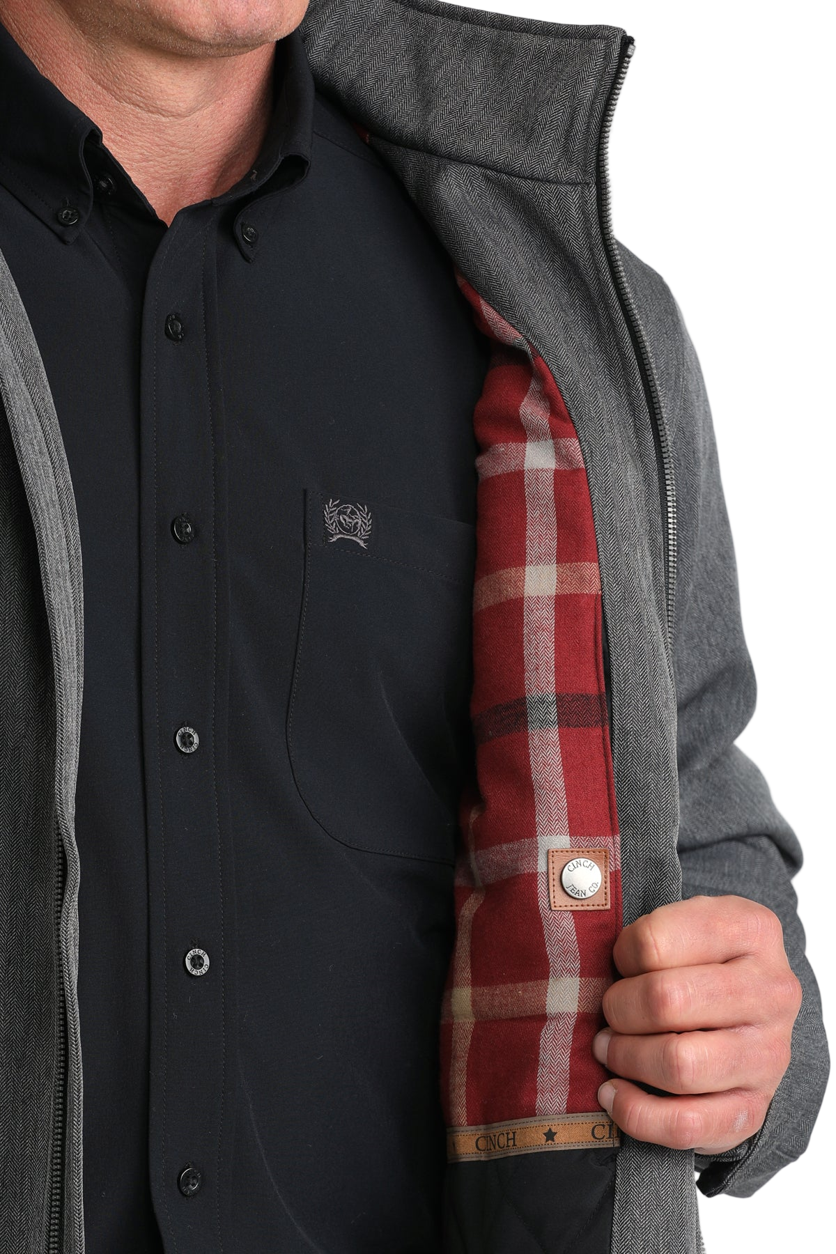 Man wearing a black button-up shirt, pulling open his grey jacket to reveal the red plaid interior lining and inner button detail