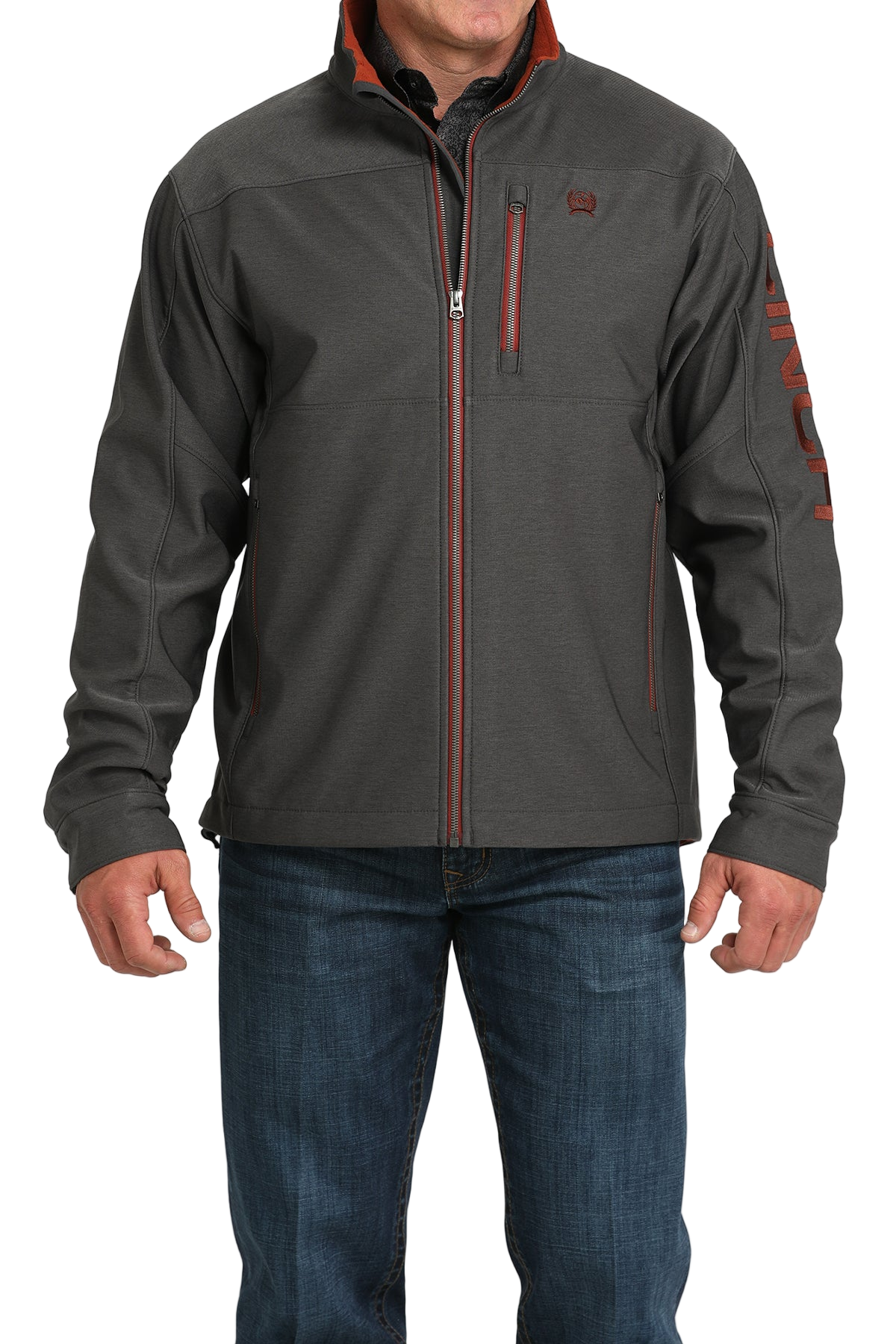 Man wearing a charcoal gray softshell jacket with bold red accents, paired with blue jeans