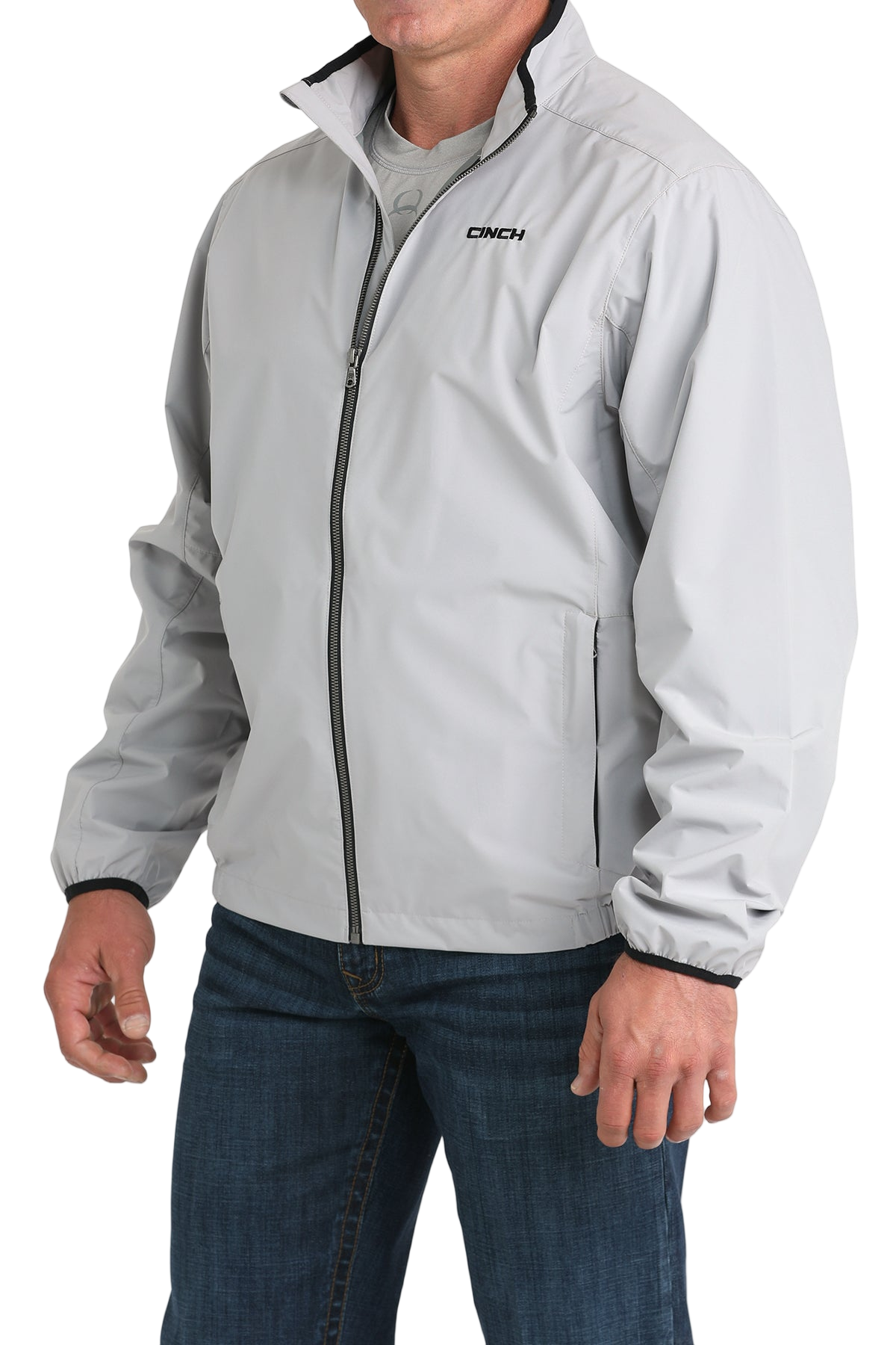 Man wearing a light gray CINCH jacket with a front zipper, paired with blue jeans