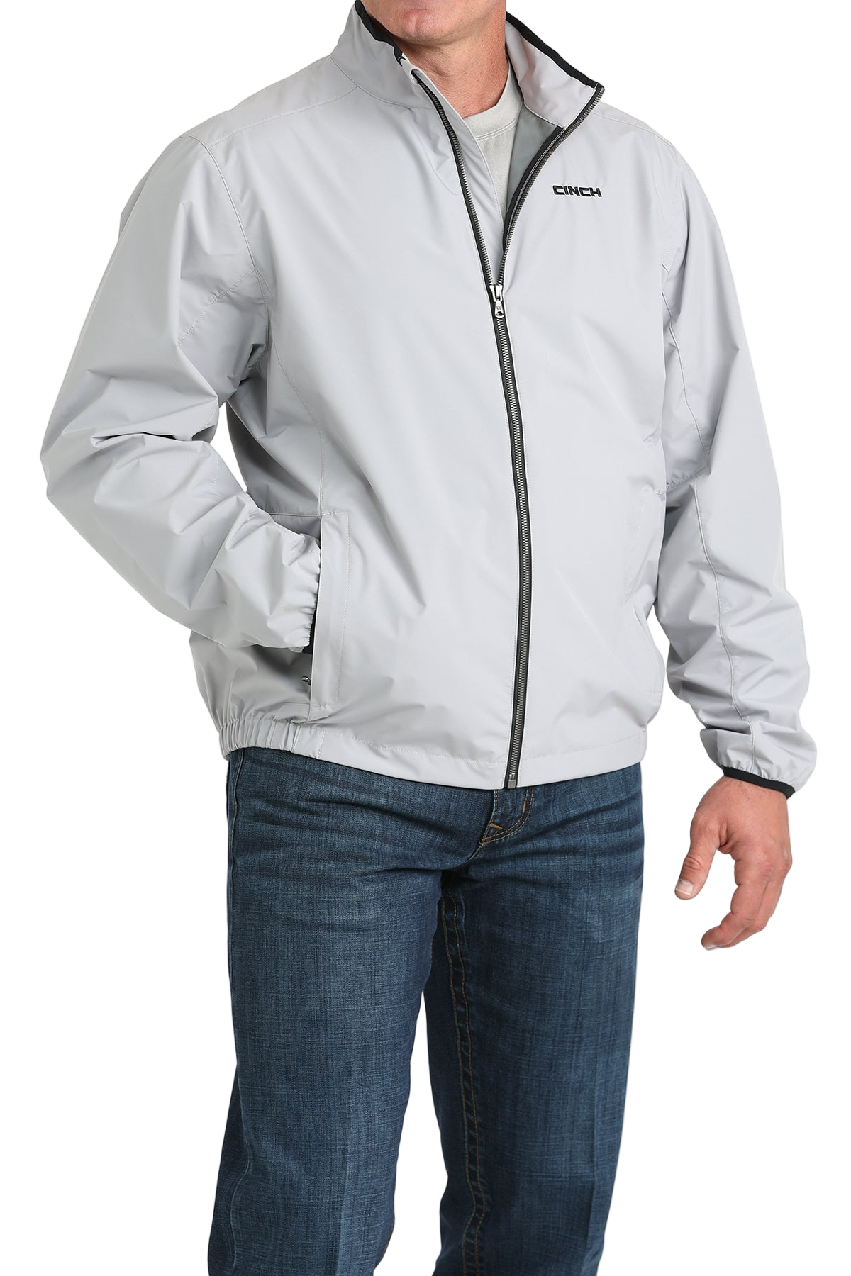 Man wearing a light gray CINCH jacket with a front zipper, paired with blue jeans
