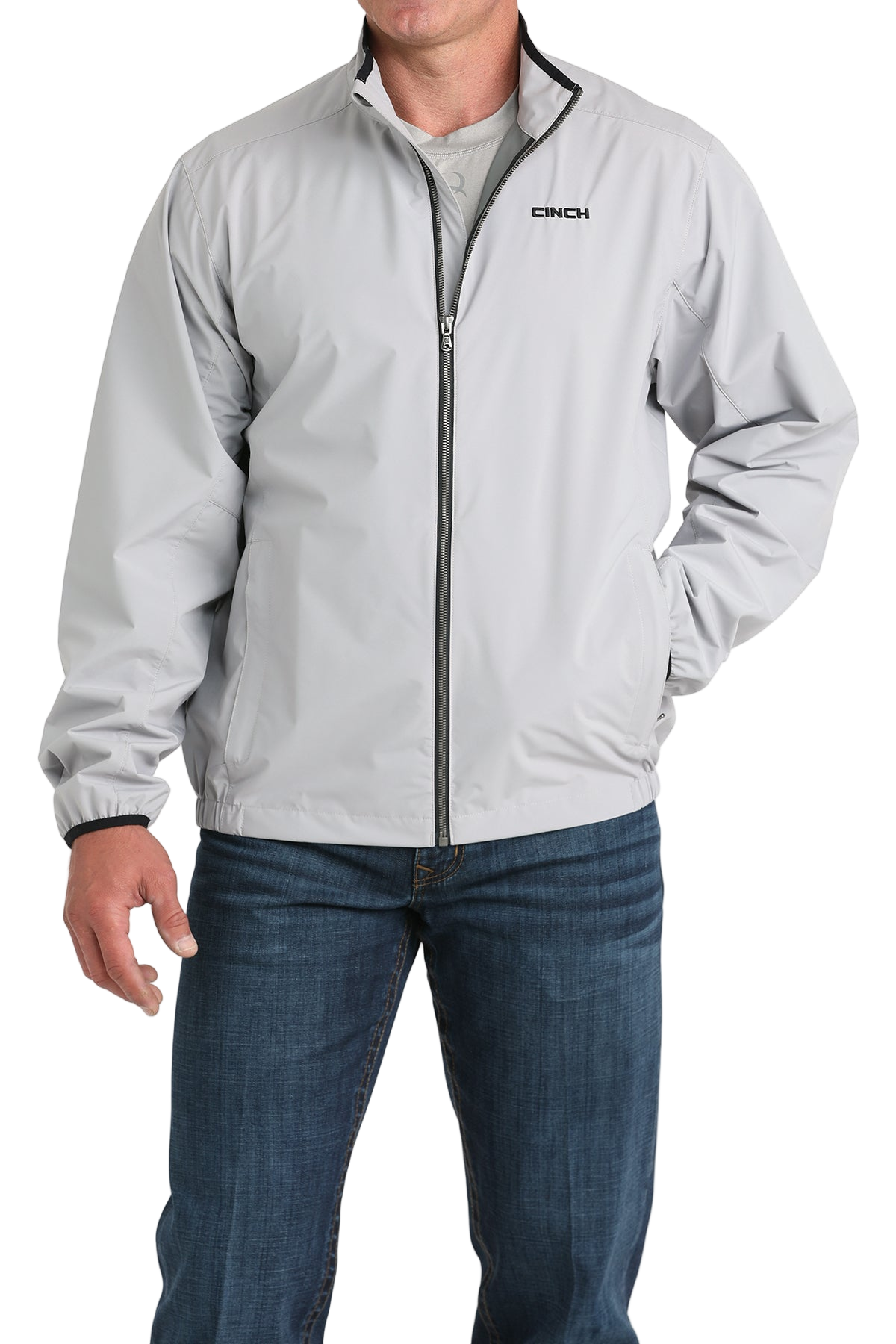 Man wearing a light gray CINCH jacket with a front zipper, paired with blue jeans