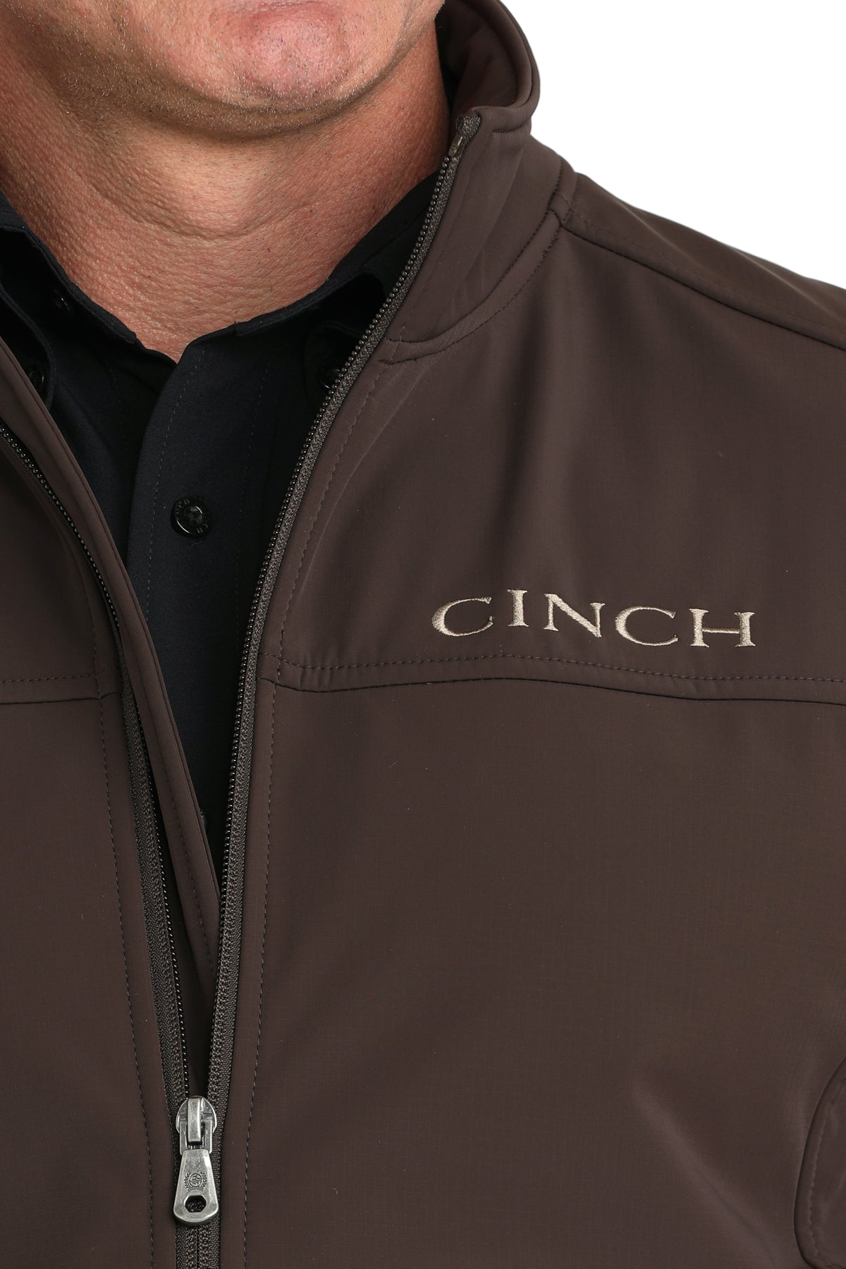 Close-up of a man wearing a brown CINCH jacket with a full front zipper, paired with a black shirt