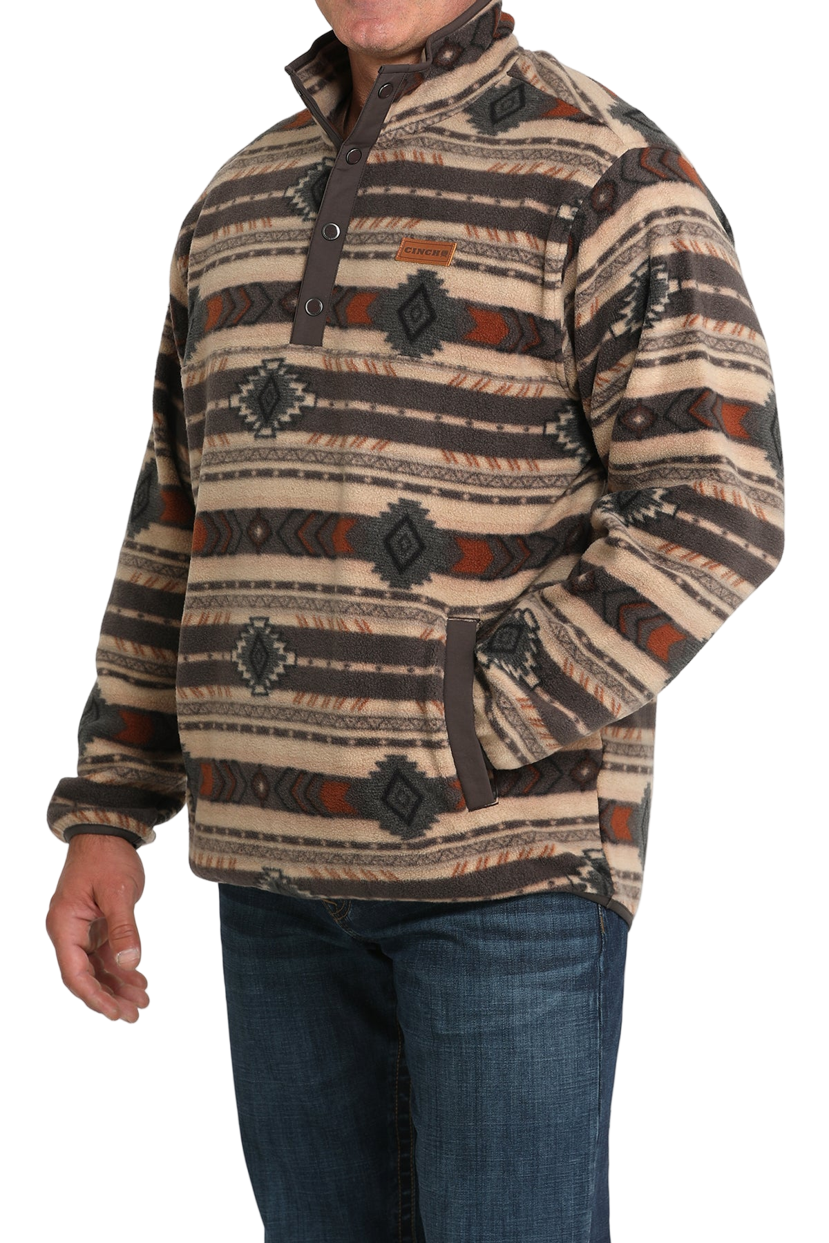Man wearing a tan and brown patterned pullover with a buttoned placket and side pockets, paired with blue jeans