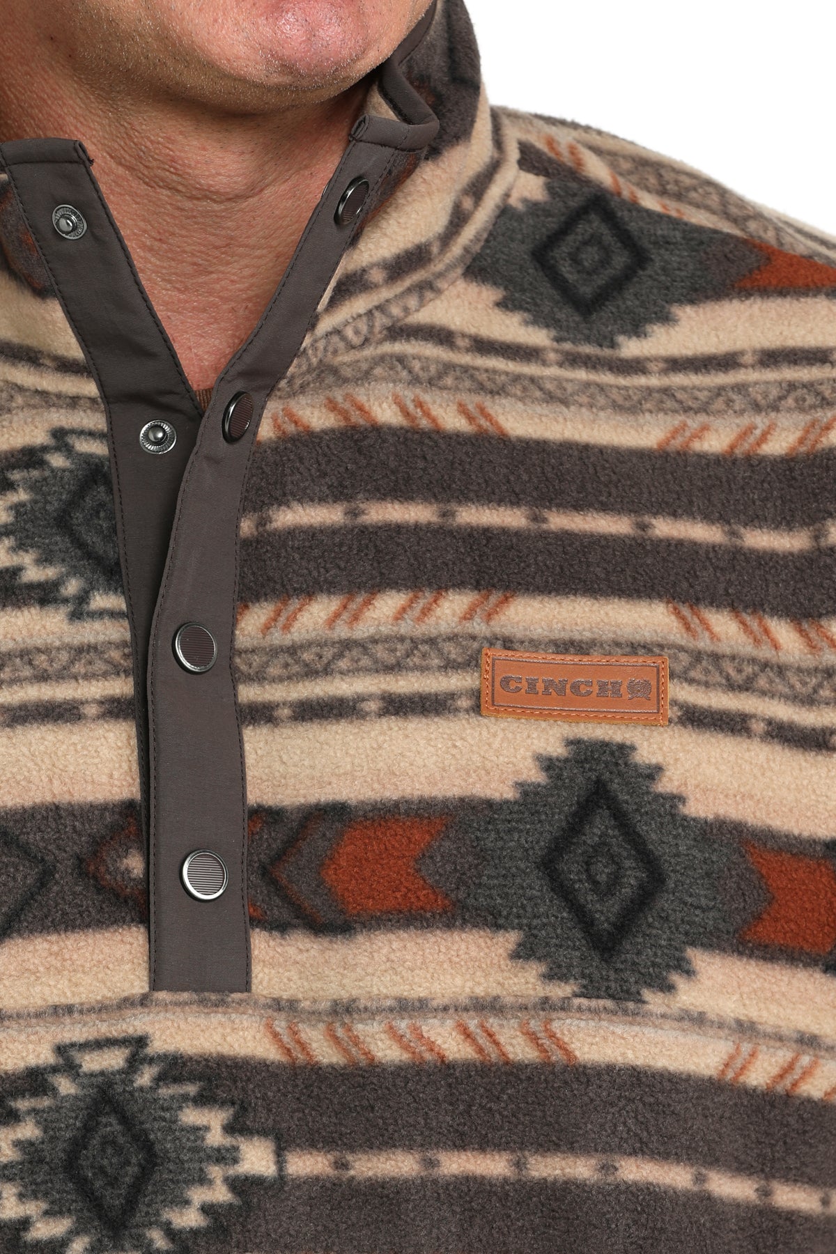 Close-up of man wearing a brown fleece pullover that has an all-over western pattern, buttons, and a 'CINCH' logo