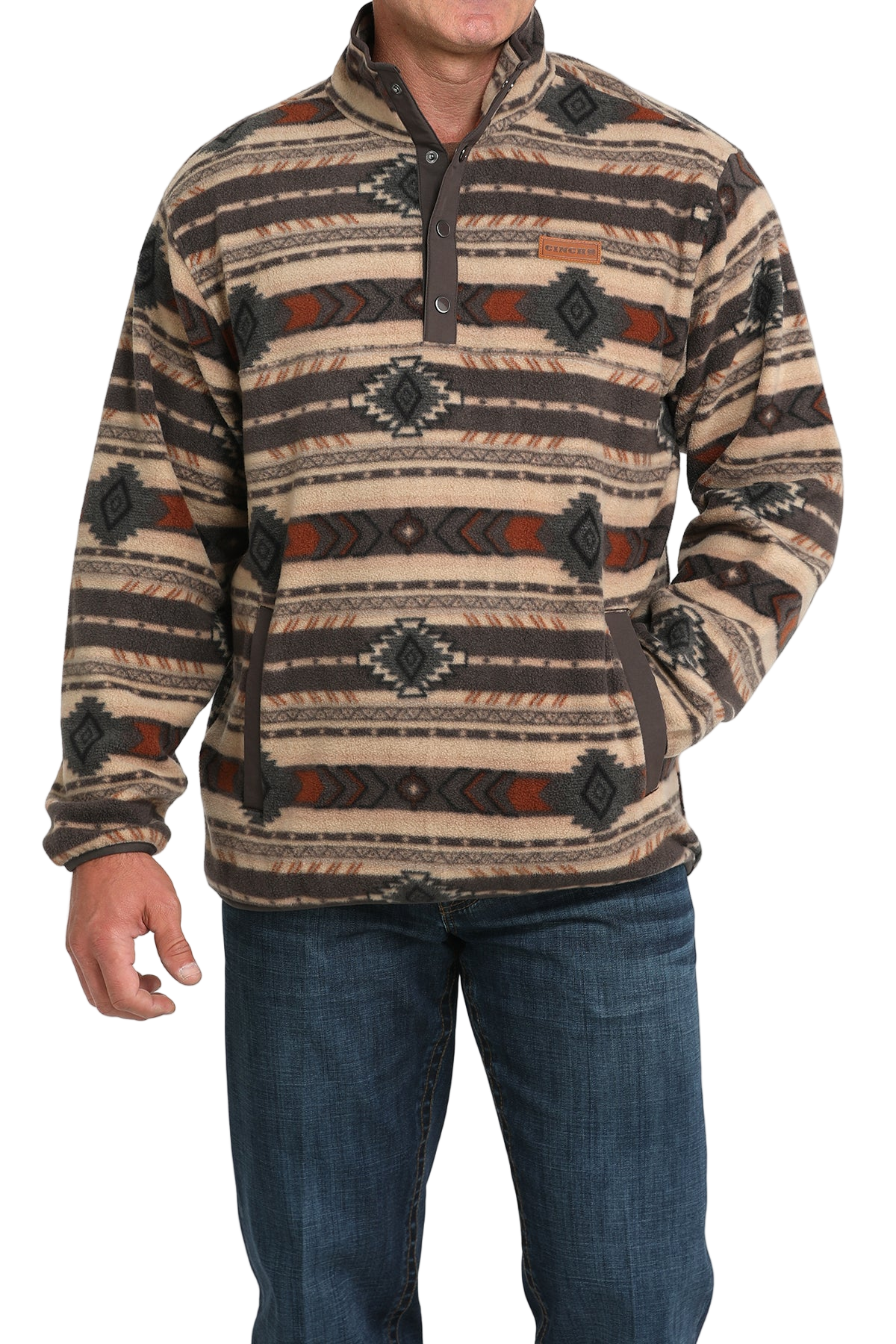 Man wearing a tan and brown patterned pullover with a buttoned placket and side pockets, paired with blue jeans