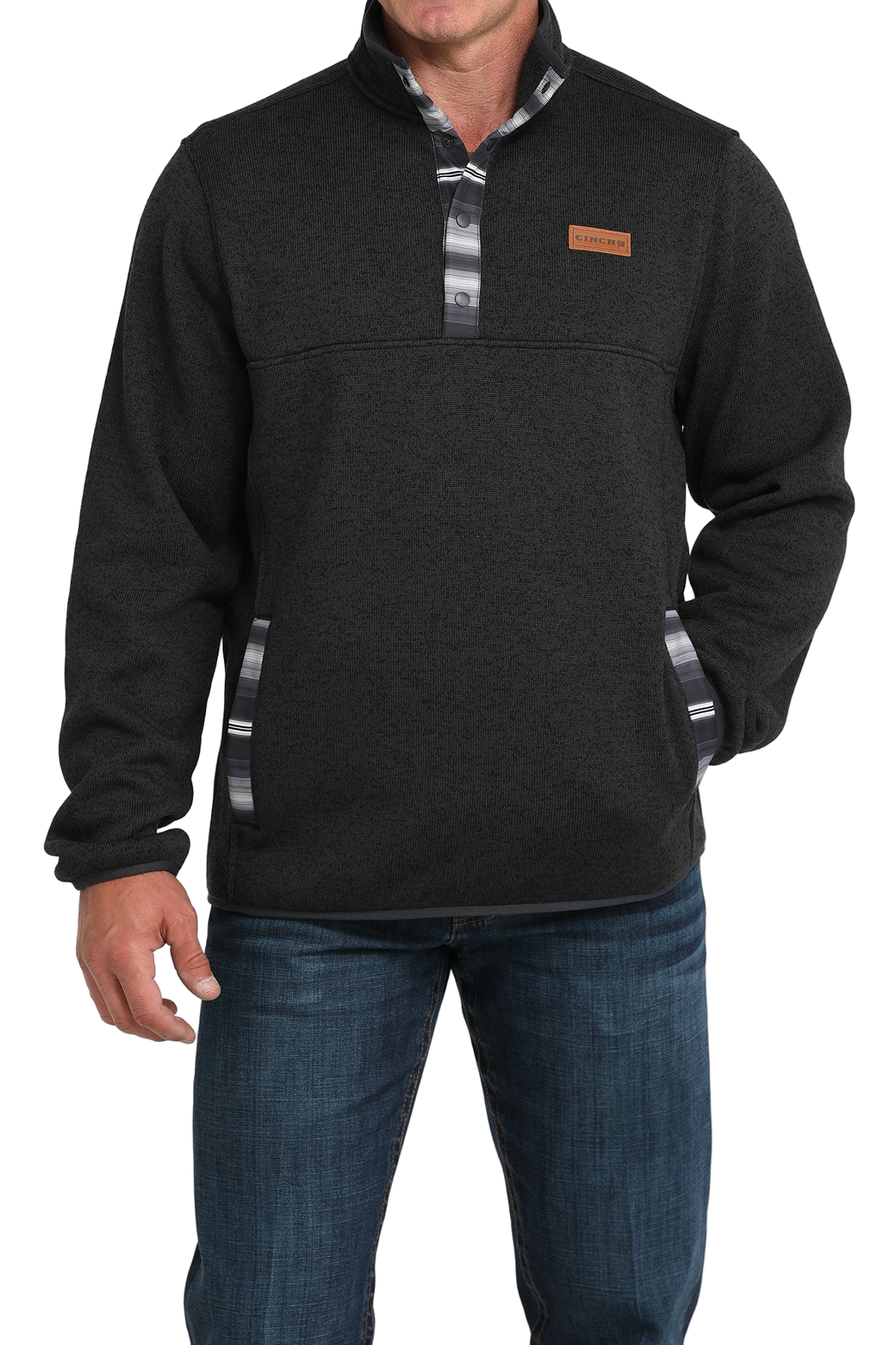 Man wearing a dark textured pullover with patterned trim on the placket and pockets, paired with blue jeans