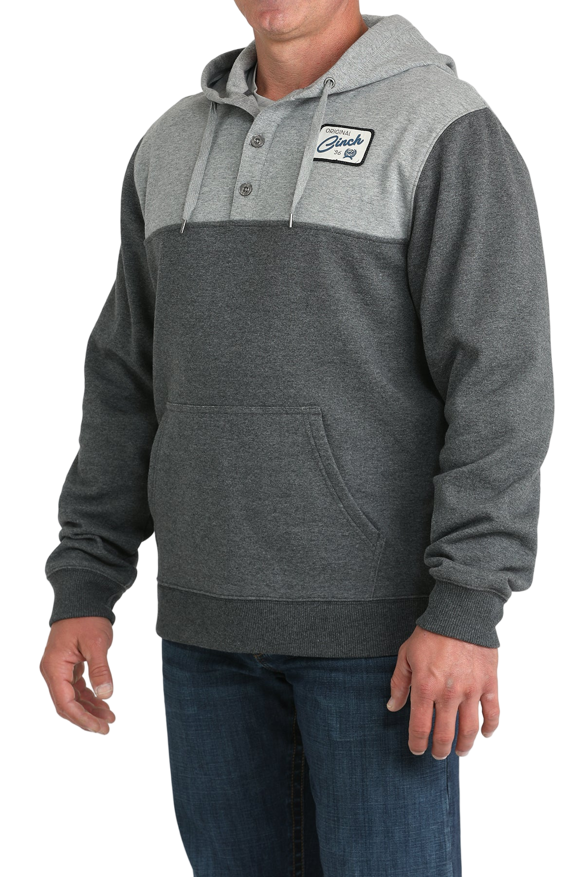 Man wearing a two-tone gray hoodie with a buttoned placket, drawstring hood, a small chest patch, and a front kangaroo pocket, paired with blue jeans