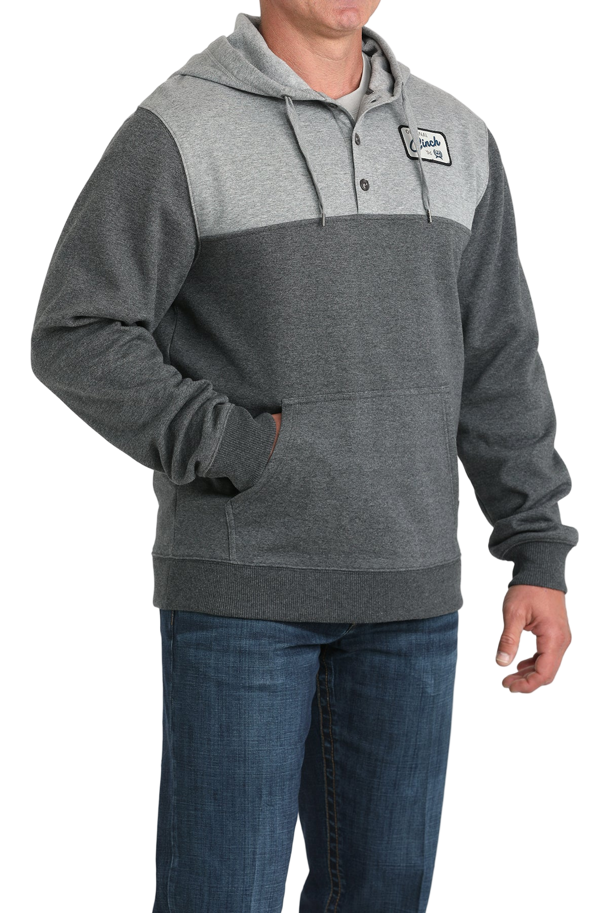 Man wearing a two-tone gray hoodie with a buttoned placket, drawstring hood, a small chest patch, and a front kangaroo pocket, paired with blue jeans