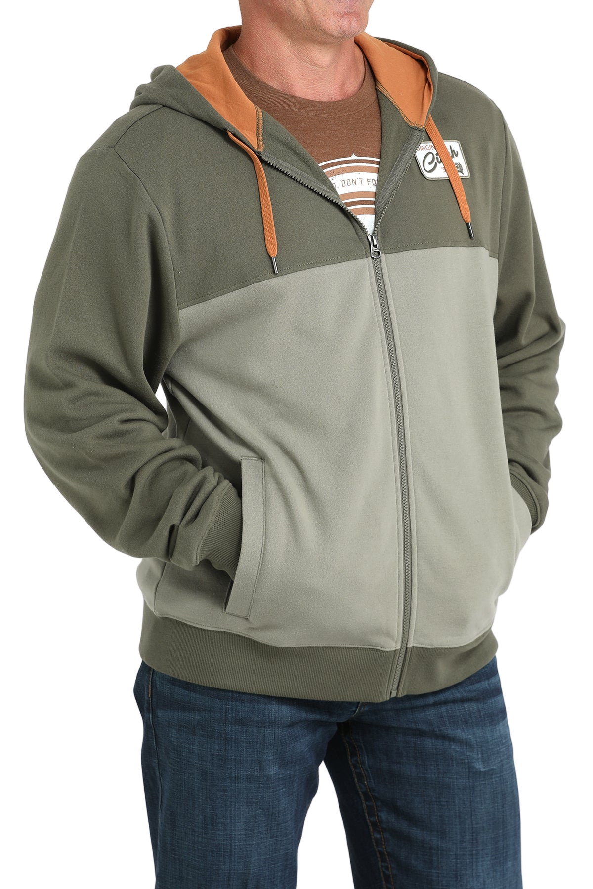 Man wearing a two-tone green zip-up hoodie with an orange hood lining and drawstrings, paired with blue jeans
