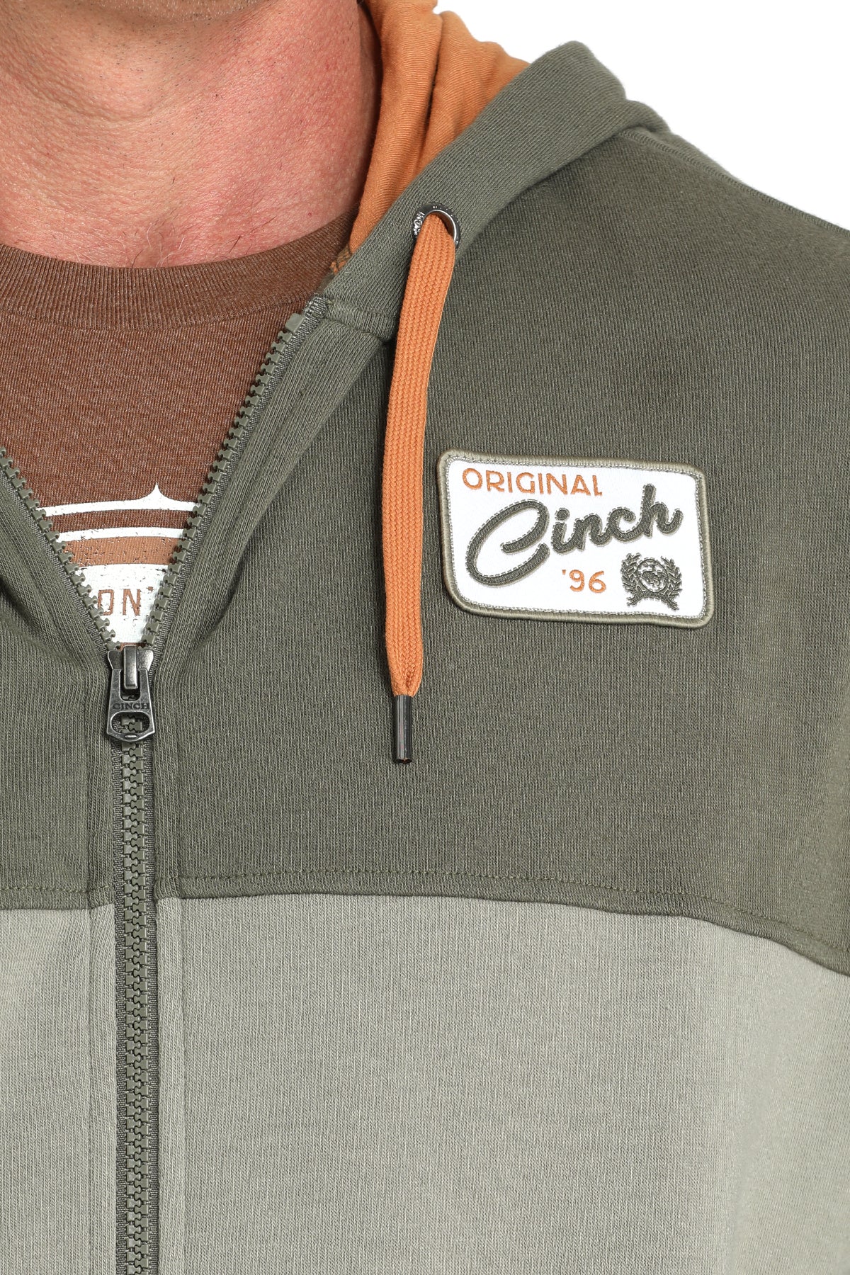 Close-up view of a man wearing a two-tone green zip-up hoodie with an orange hood lining displayed on a white background.