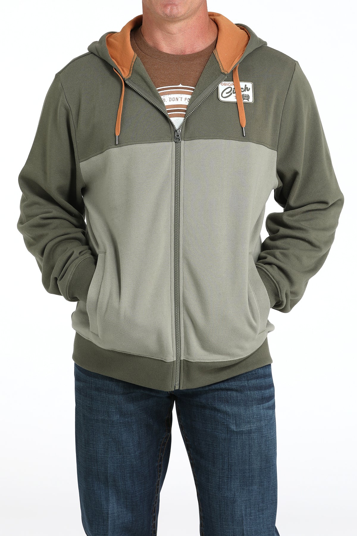 Man wearing a two-tone green zip-up hoodie with an orange hood lining and blue jeans displayed on a white background.