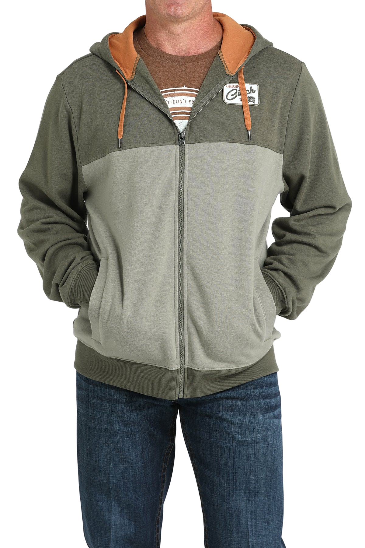 Man wearing a two-tone green zip-up hoodie with an orange hood lining and drawstrings, paired with blue jeans