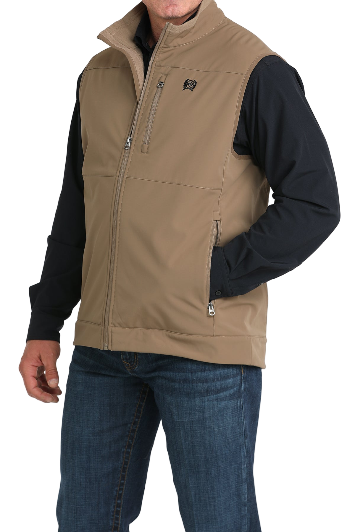 Man wearing a tan zip-up vest over a black long-sleeve shirt and jeans