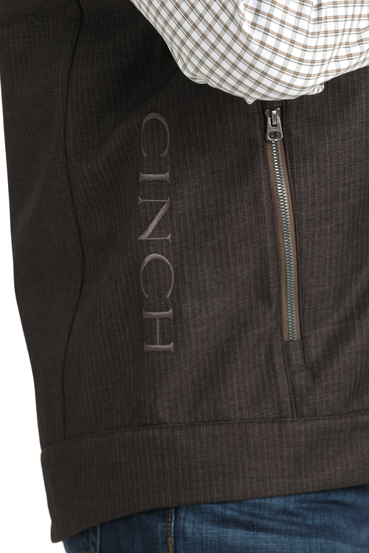 Close-up of a man wearing a dark brown vest with a vertical CINCH logo on the side, shown over a checked long-sleeve shirt