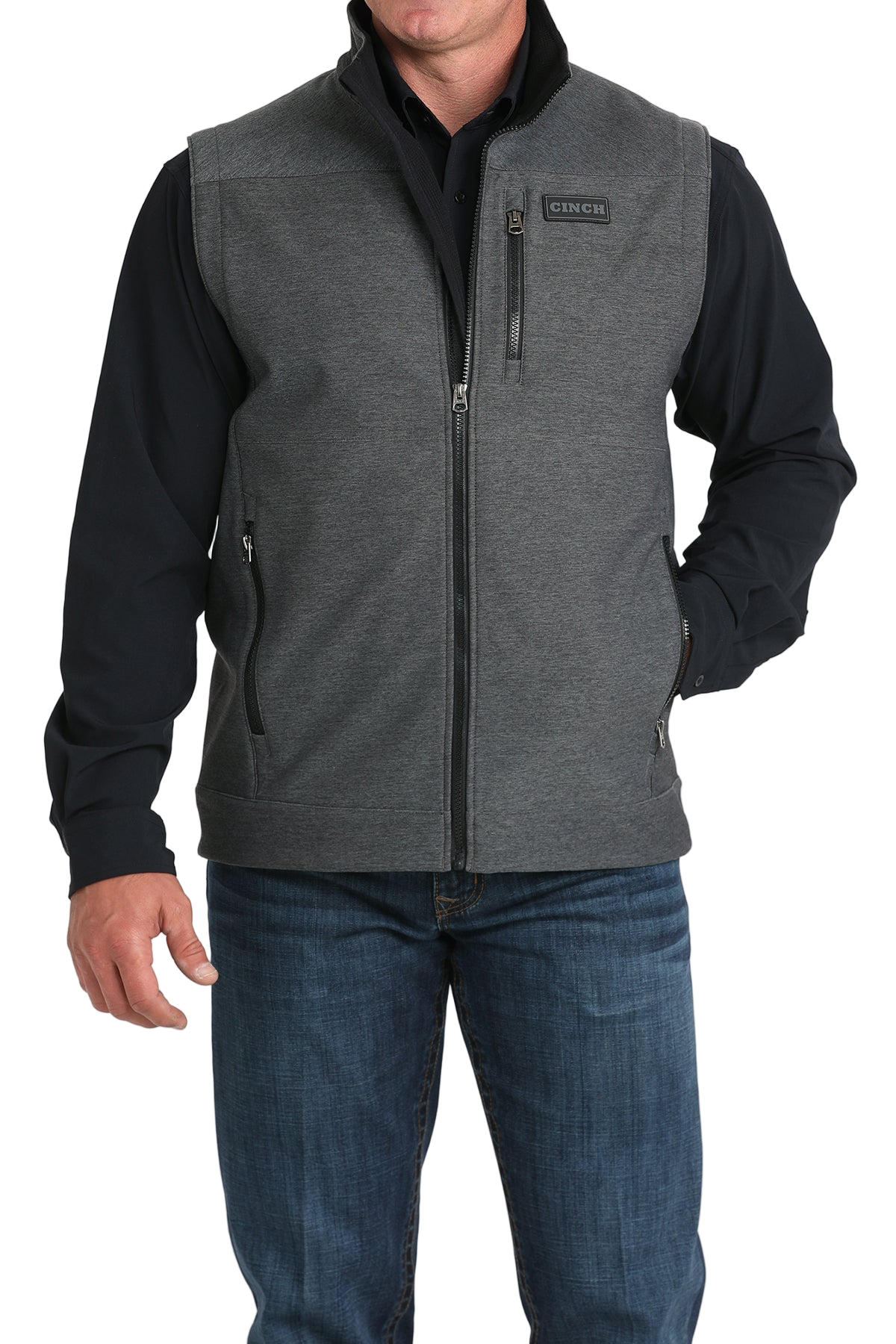 Man wearing a gray zip-up vest over a black long-sleeve shirt and jeans