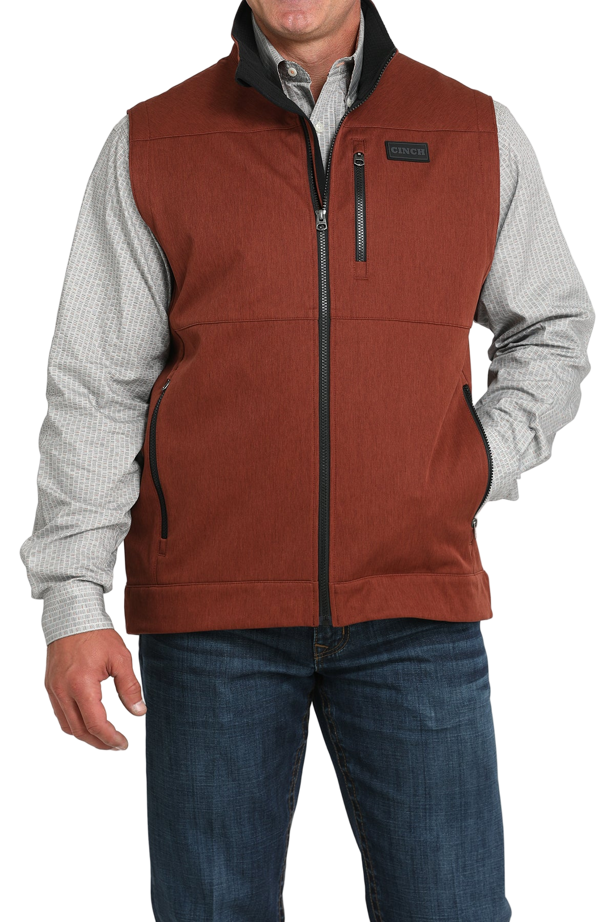 Man wearing a rust orange zip-up vest over a white long-sleeve shirt and jeans