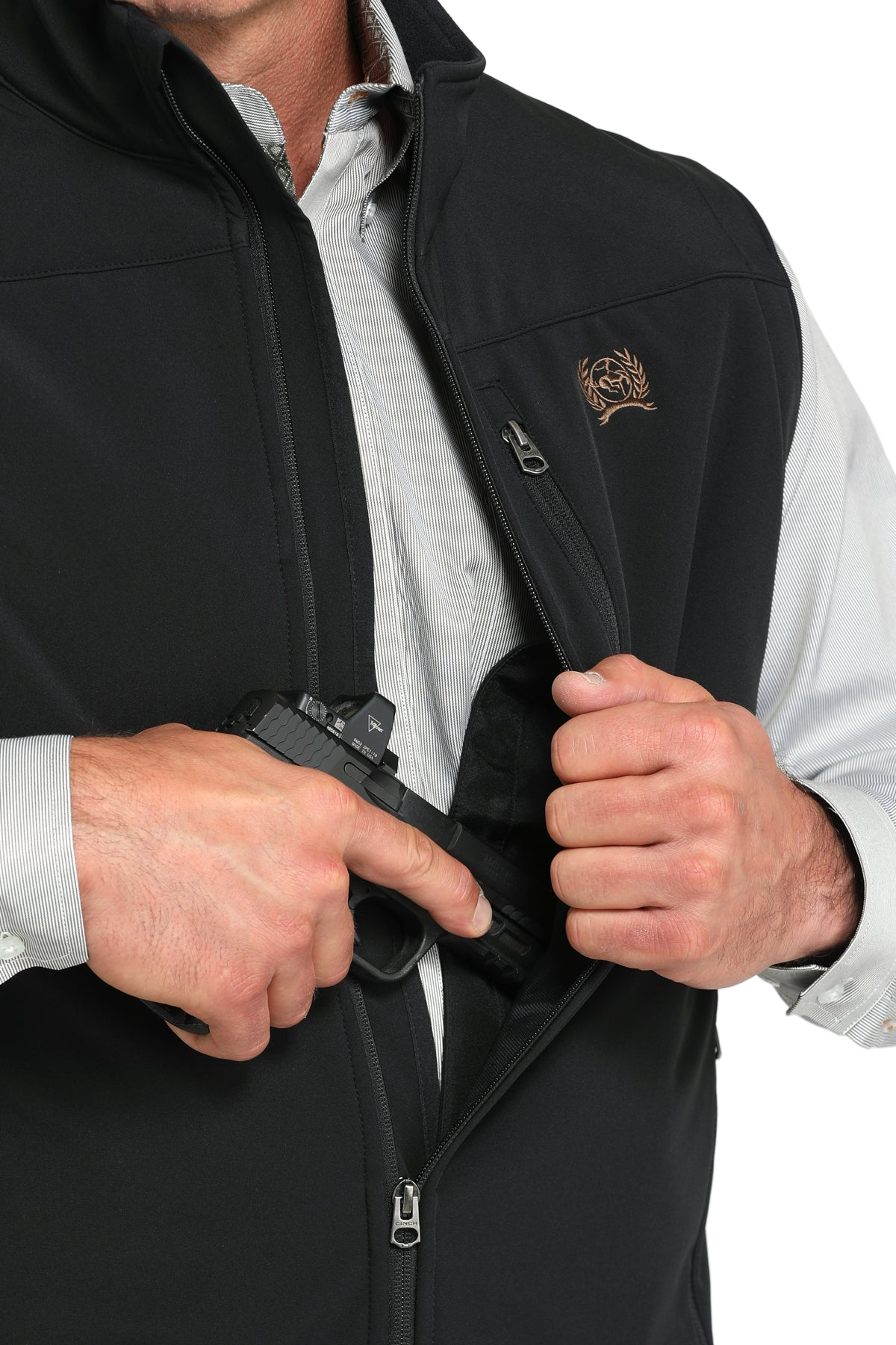 A man opens the front of a black vest to reveal an interior concealed-carry pocket, with one hand gripping a holstered handgun inside. A striped button-up shirt is visible underneath