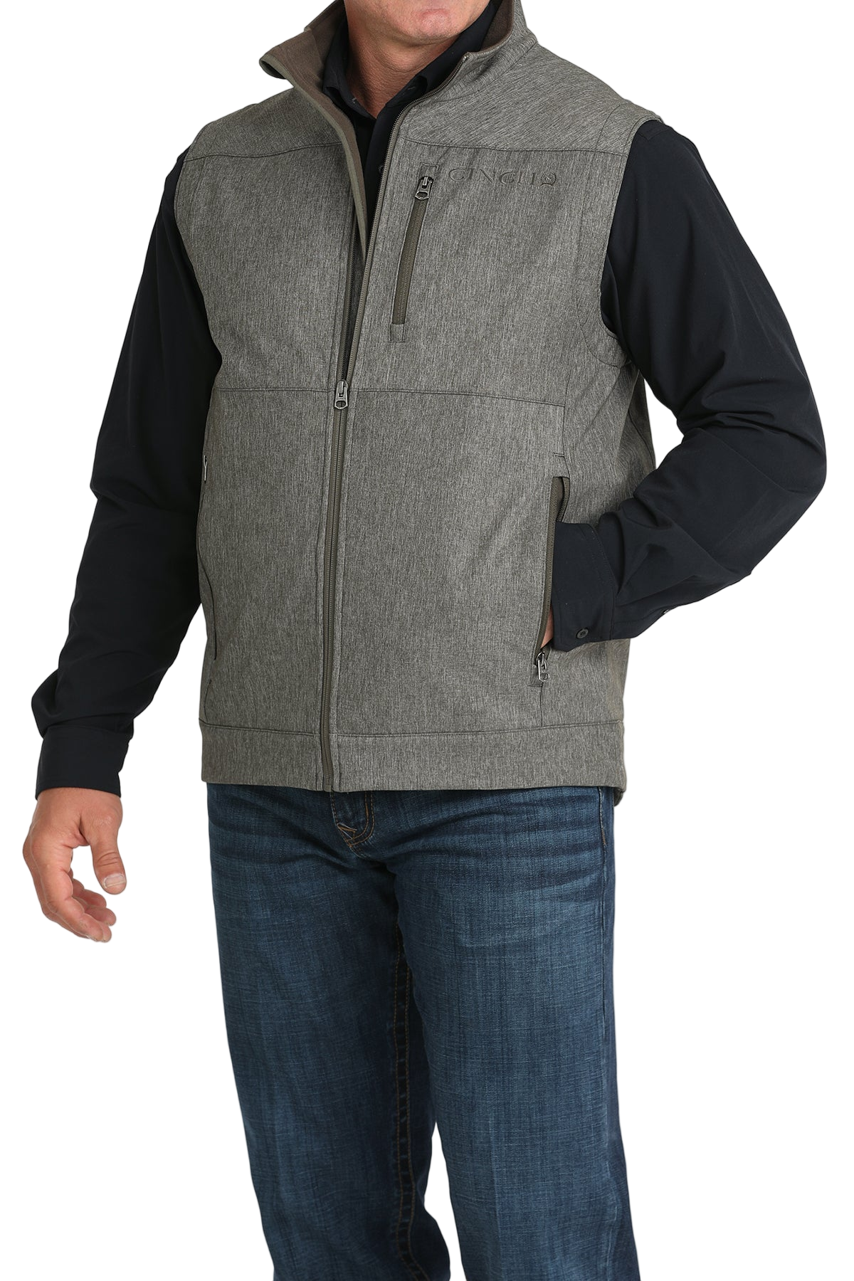 A man wearing a gray zip-up vest over a black shirt, paired with blue jeans