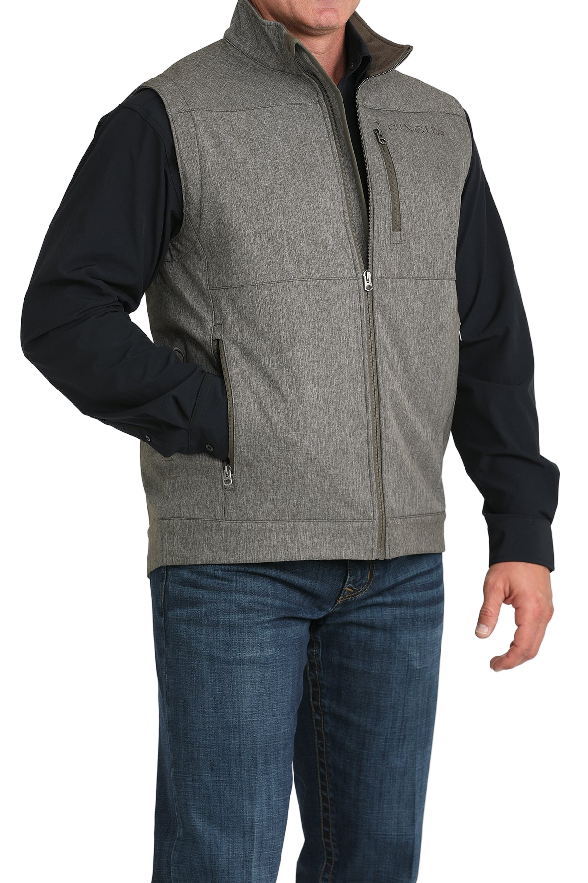 A man wearing a gray zip-up vest over a black shirt, paired with blue jeans