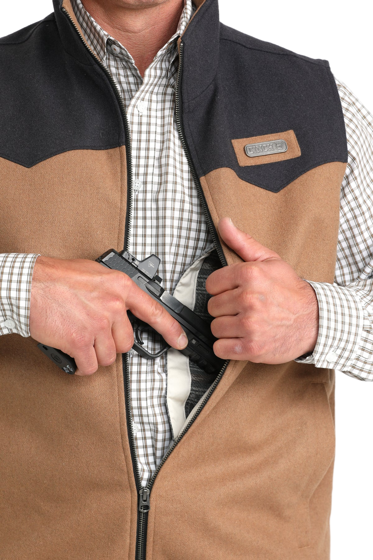 A man in a two-tone vest and plaid shirt unzips the front to reveal an inside concealed-carry pocket holding a handgun