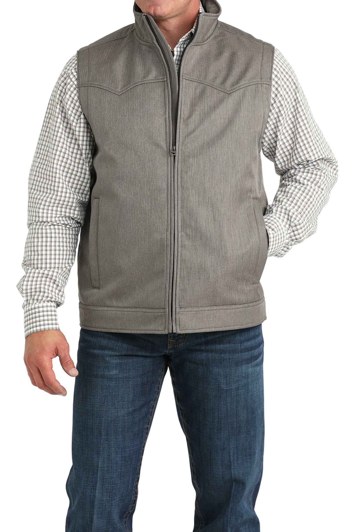 A man wearing a light gray zip-up vest over a white and brown checkered button-down shirt, paired with blue jeans