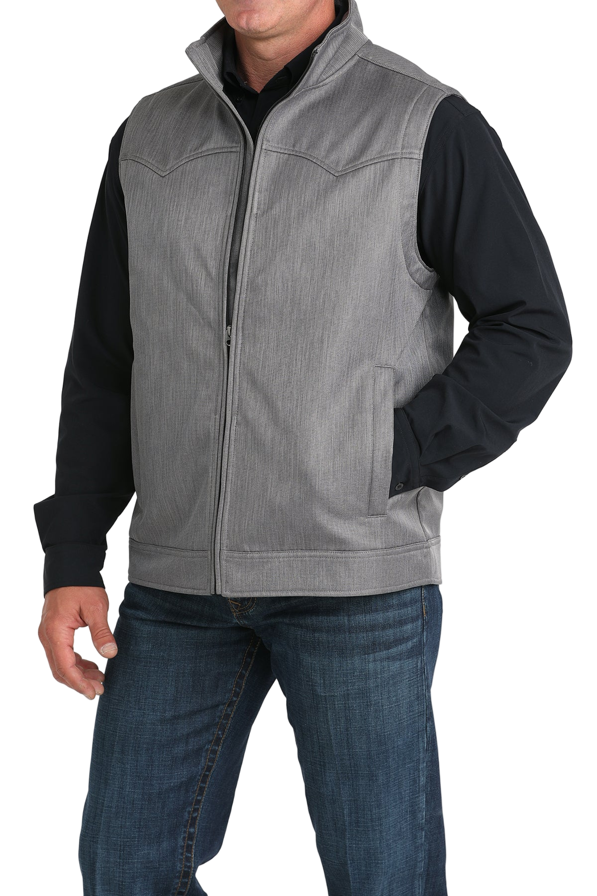 A man wears a light gray zip-front vest over a black long-sleeve shirt and blue jeans