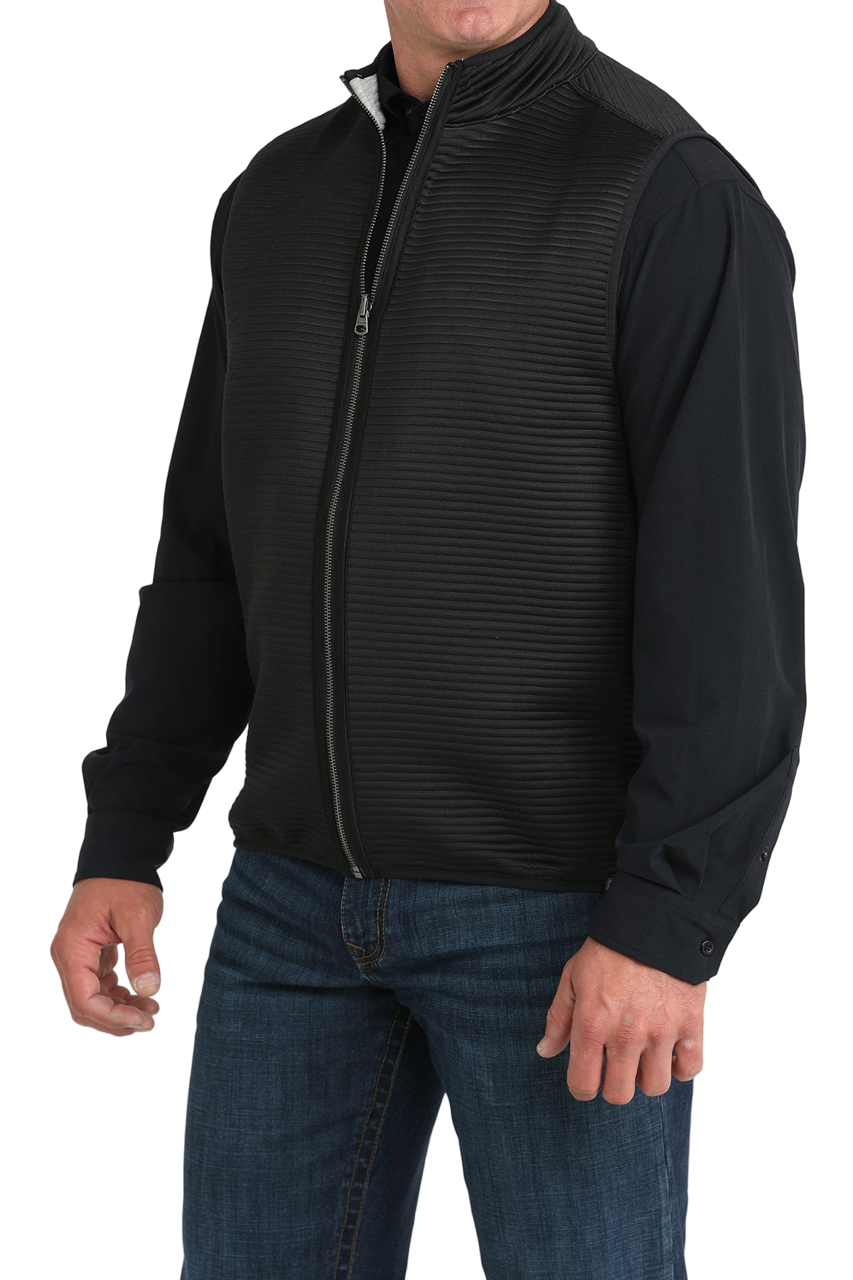 A man wears a black zip-front vest over a black long-sleeve shirt and blue jeans