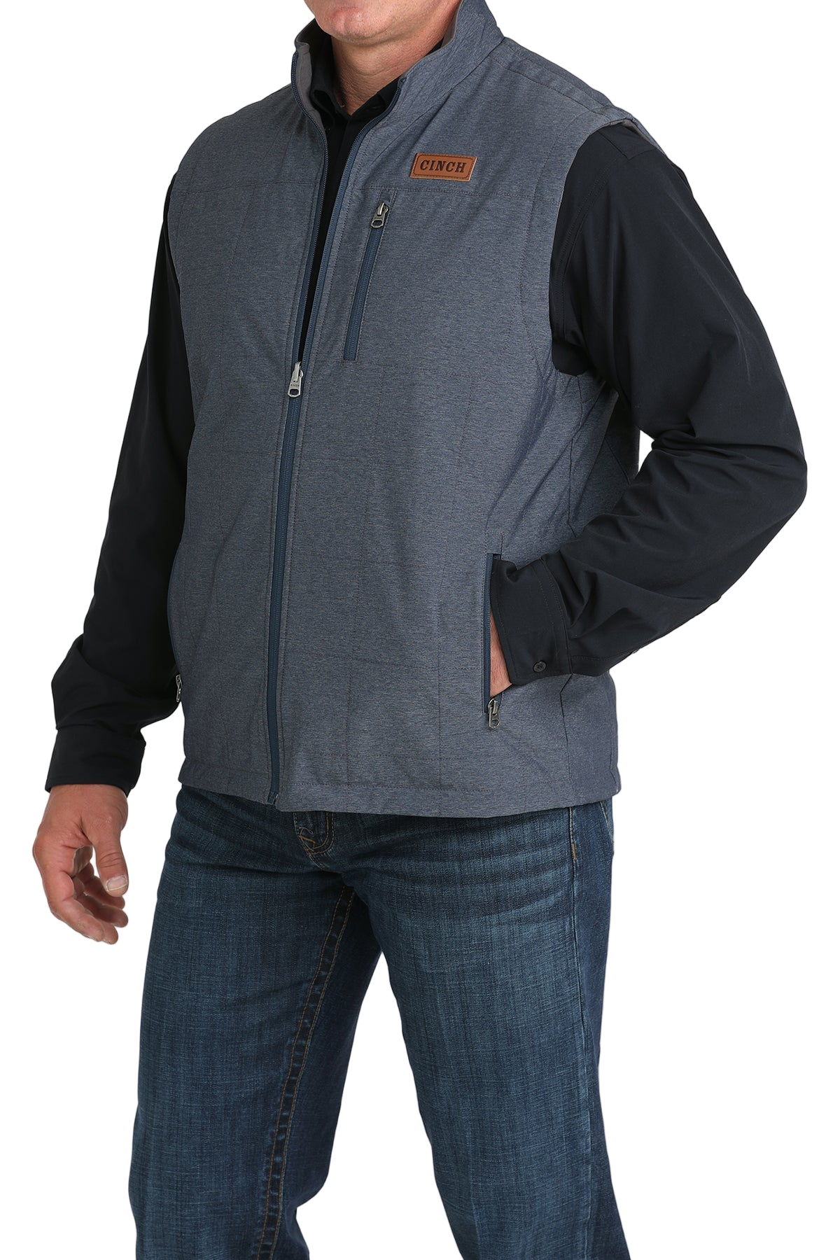 A man wearing a blue zip-up vest over a black shirt, paired with blue jeans