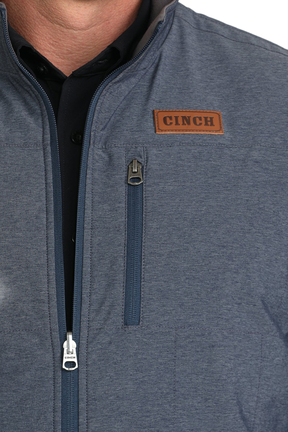 Close-up of a man wearing a blue zip-up vest over a black shirt