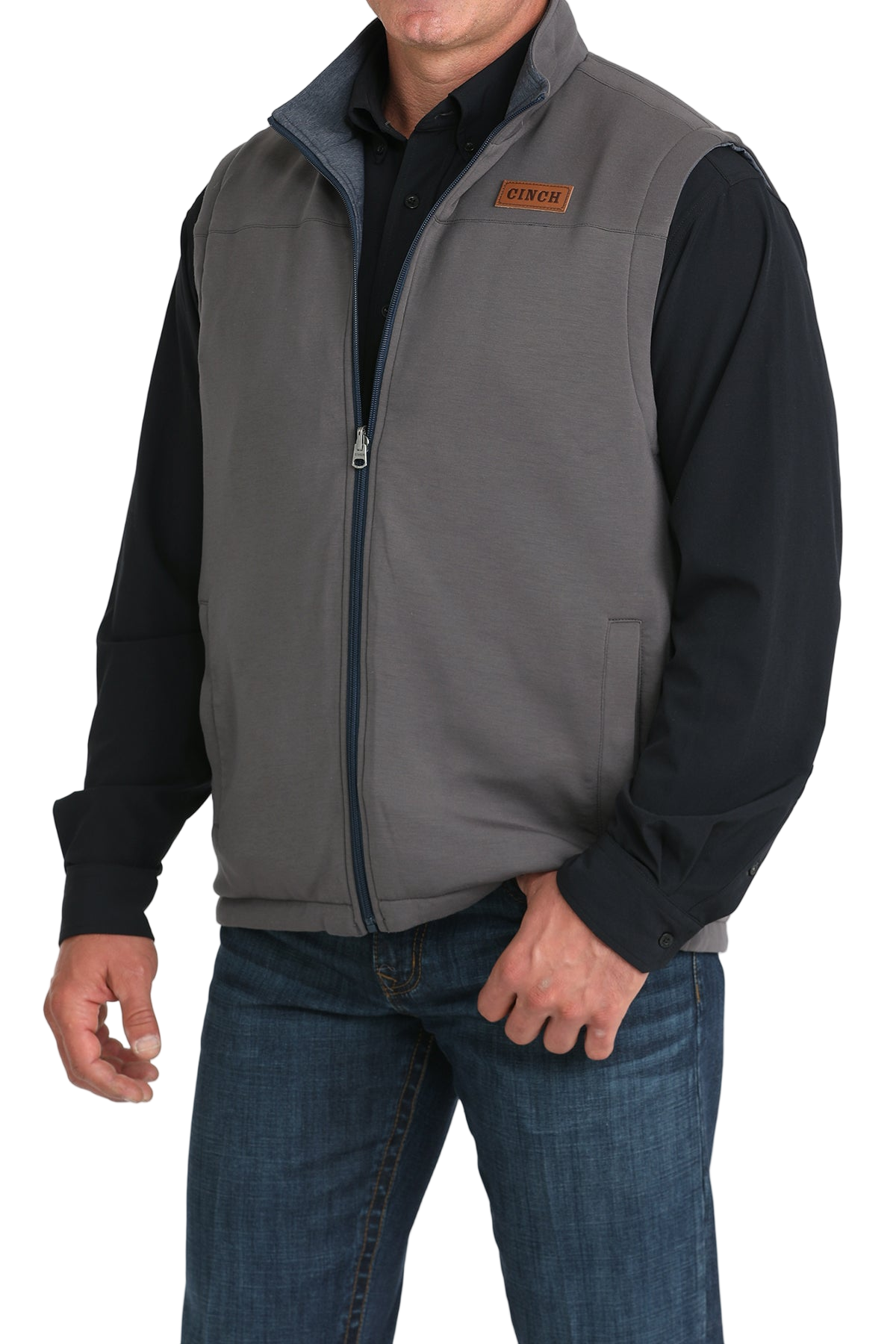 A man wearing a gray zip-up vest over a black shirt, paired with blue jeans