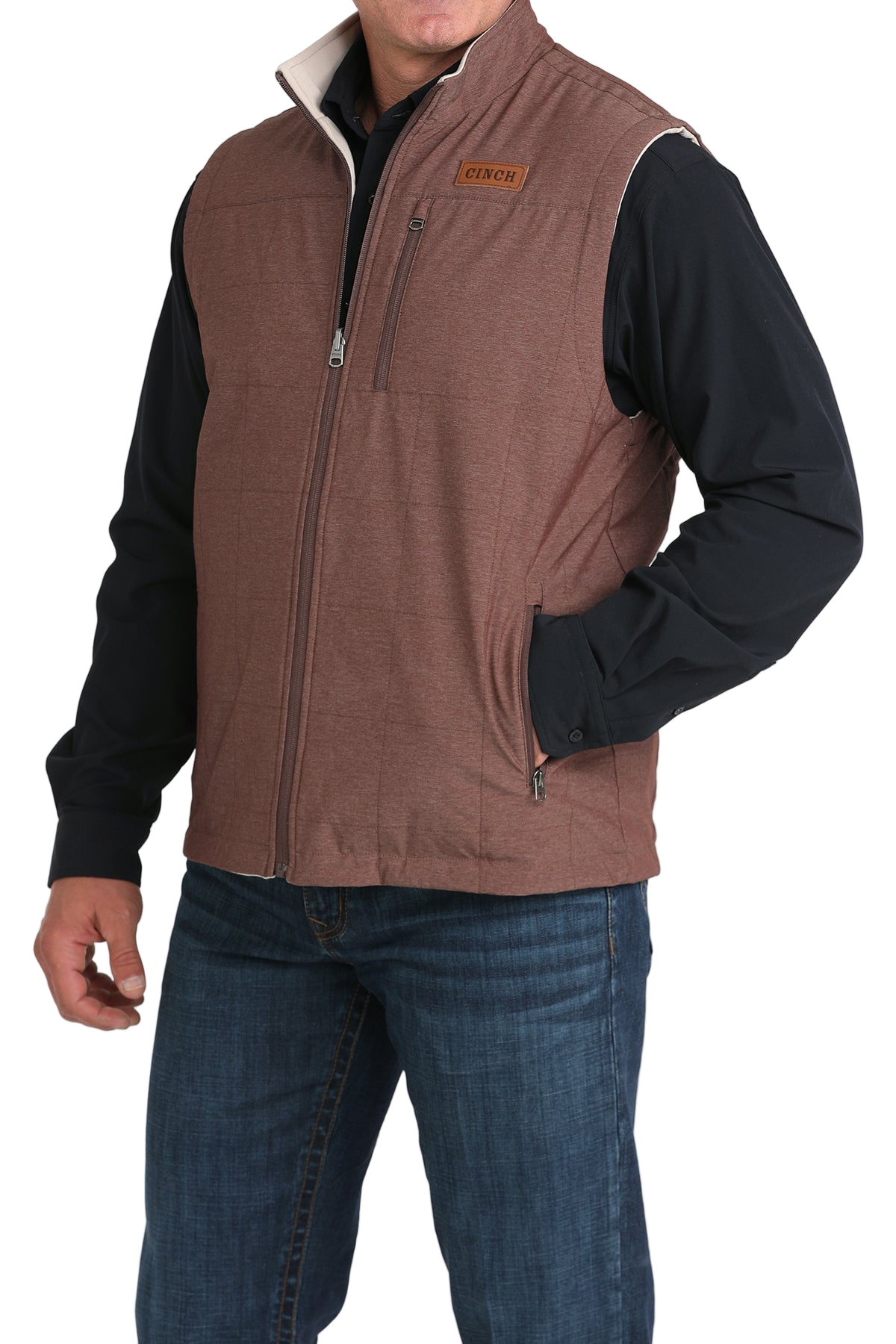 A man wears a maroon zip-front vest over a black long-sleeve shirt and blue jeans