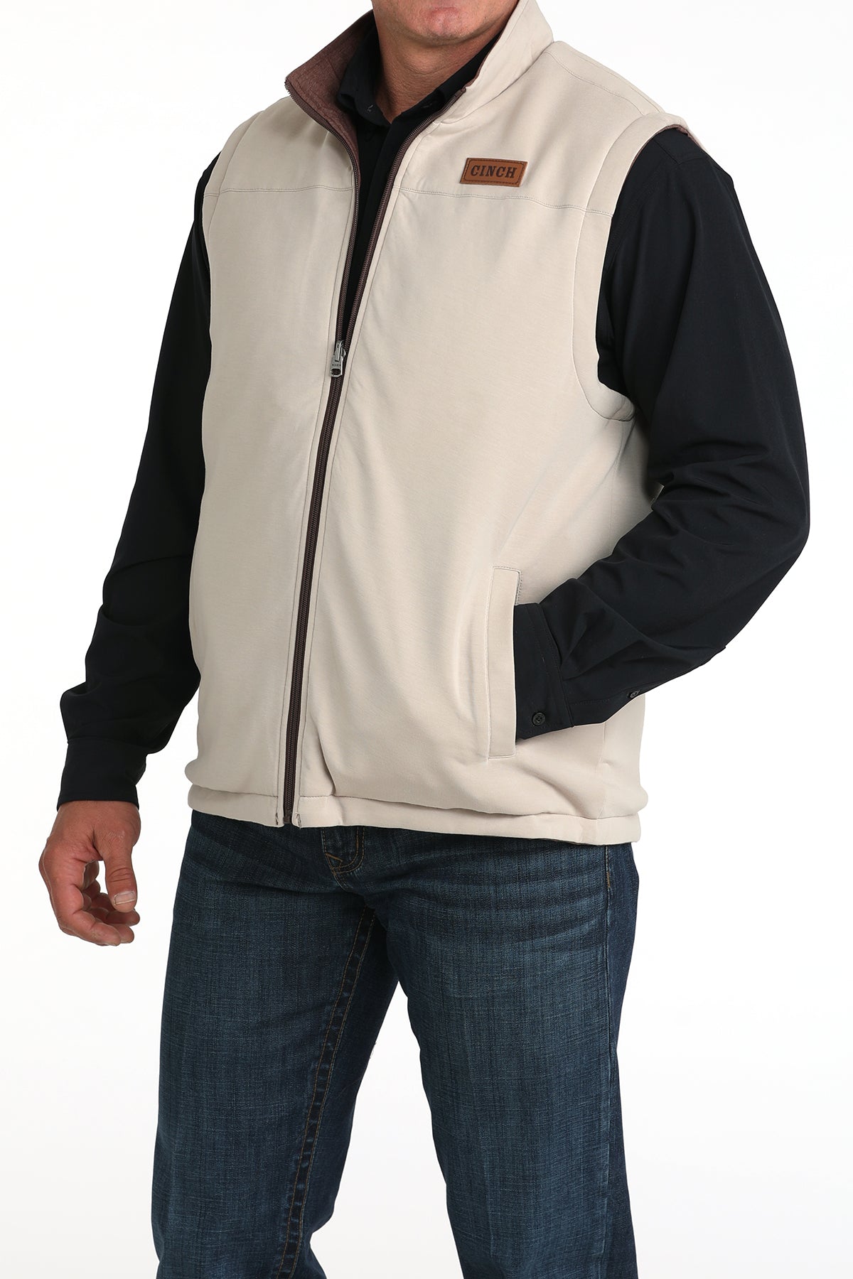 Man wearing a beige vest with a black undershirt and jeans