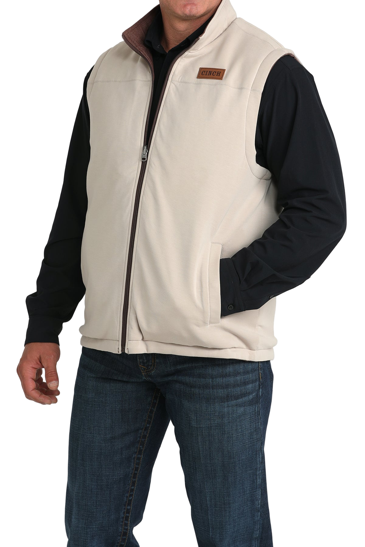 A man wears a white zip-front vest over a black long-sleeve shirt and blue jeans