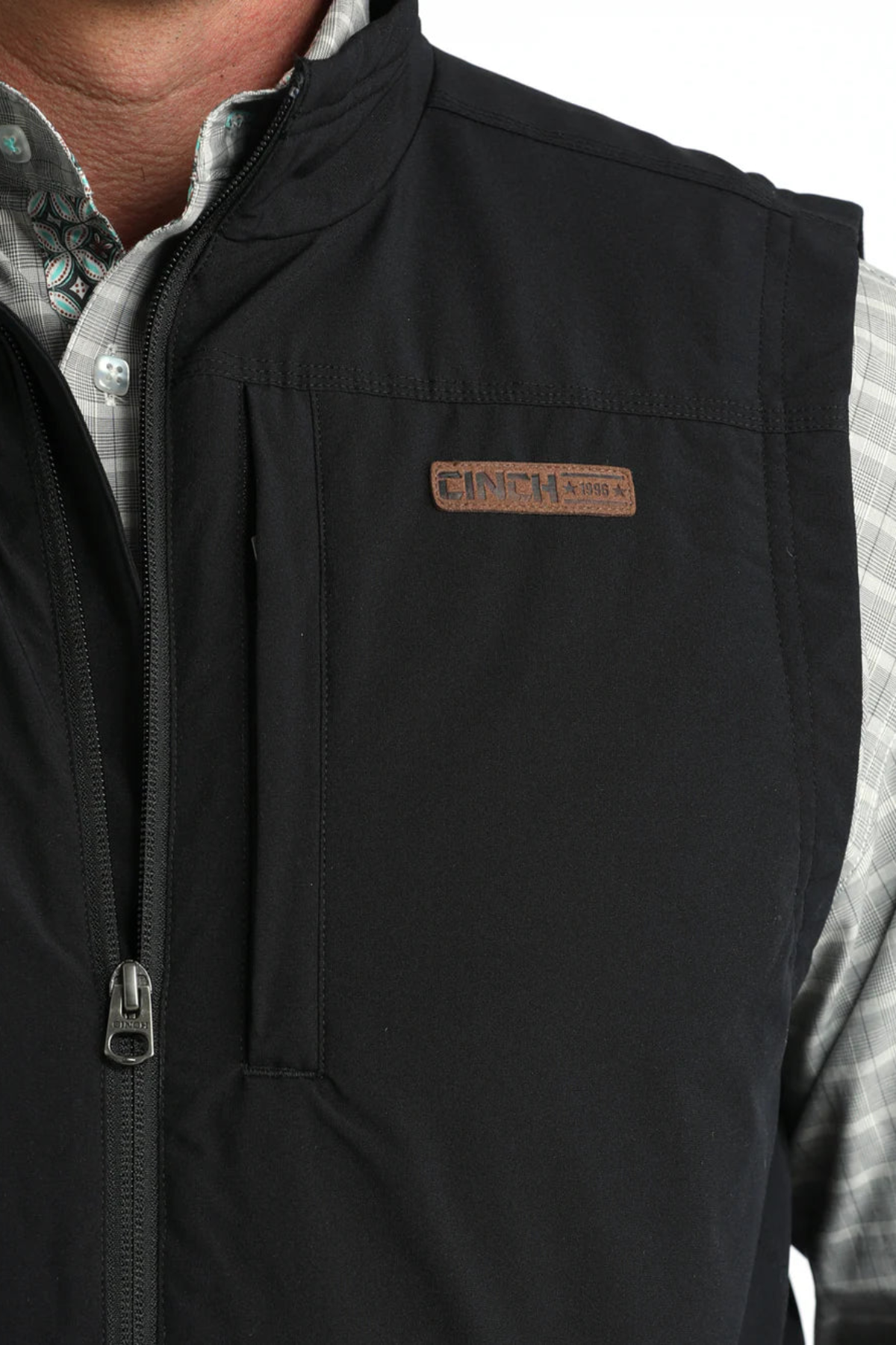 Black vest with a brand logo on a person wearing a plaid shirt.
