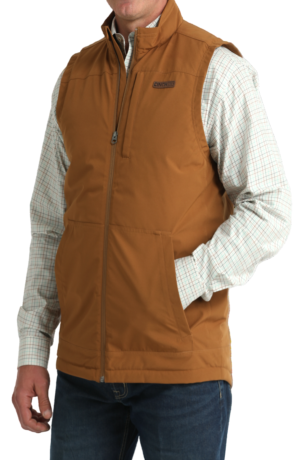 A man wearing a tan zip-up vest over a light plaid button-down shirt, paired with blue jeans