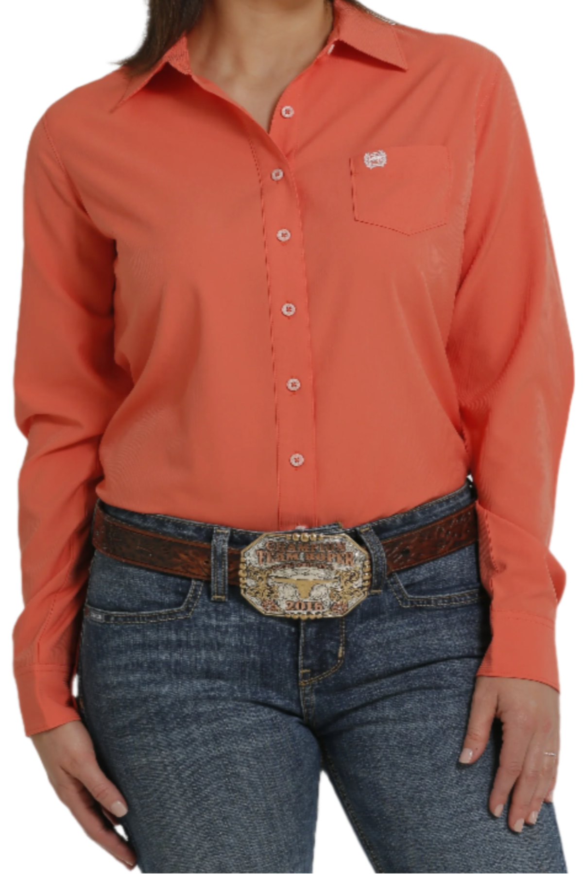 A woman wearing a long-sleeve coral Western shirt with a button-down collar, paired with blue jeans and a belt with a decorative buckle.