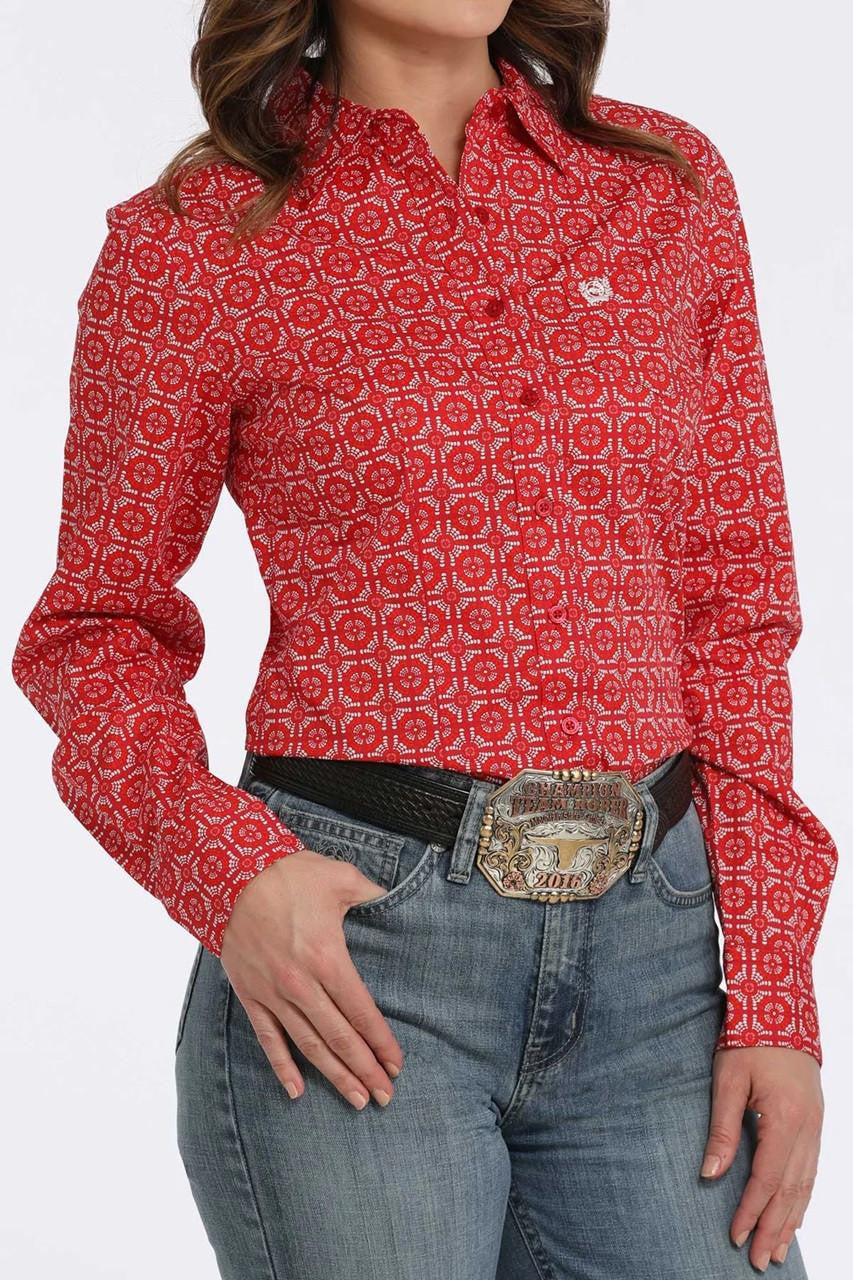 Woman wearing a red printed long sleeve button-down shirt with blue jeans and a belt buckle on a white background