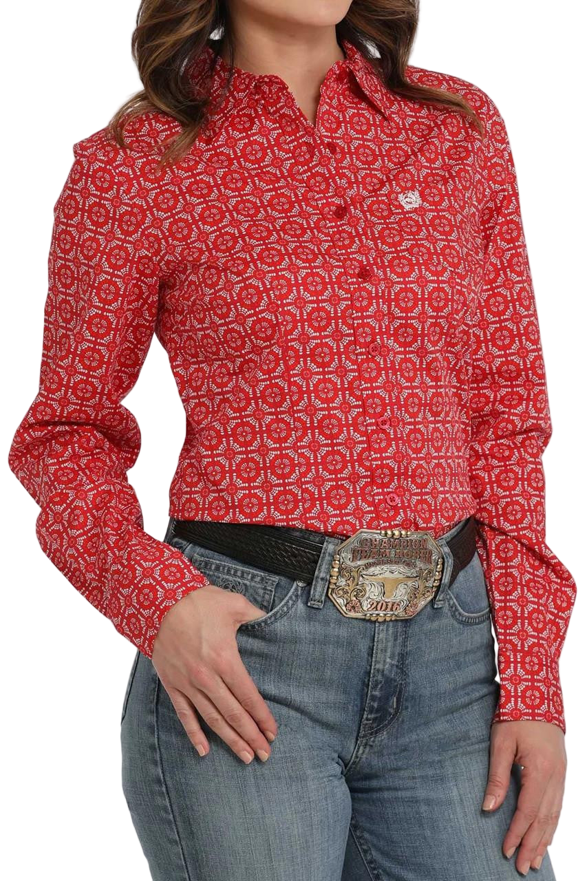Woman wearing a bright red long-sleeve button-down shirt with an allover geometric print, paired with light-wash jeans and a large silver western belt buckle