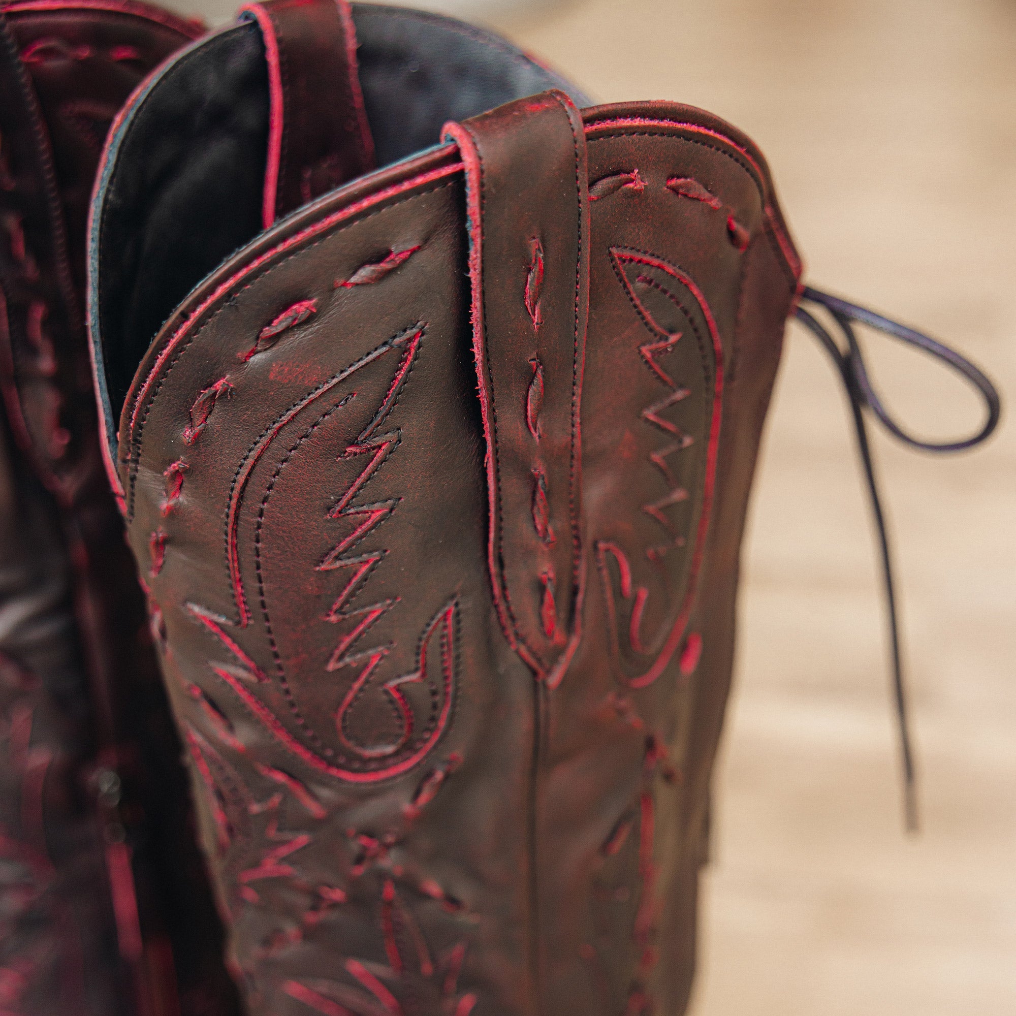 Close-up of dark red cowboy boot with red stitching and detailing, showing the pull strap and decorative embroidery near the top of the shaft