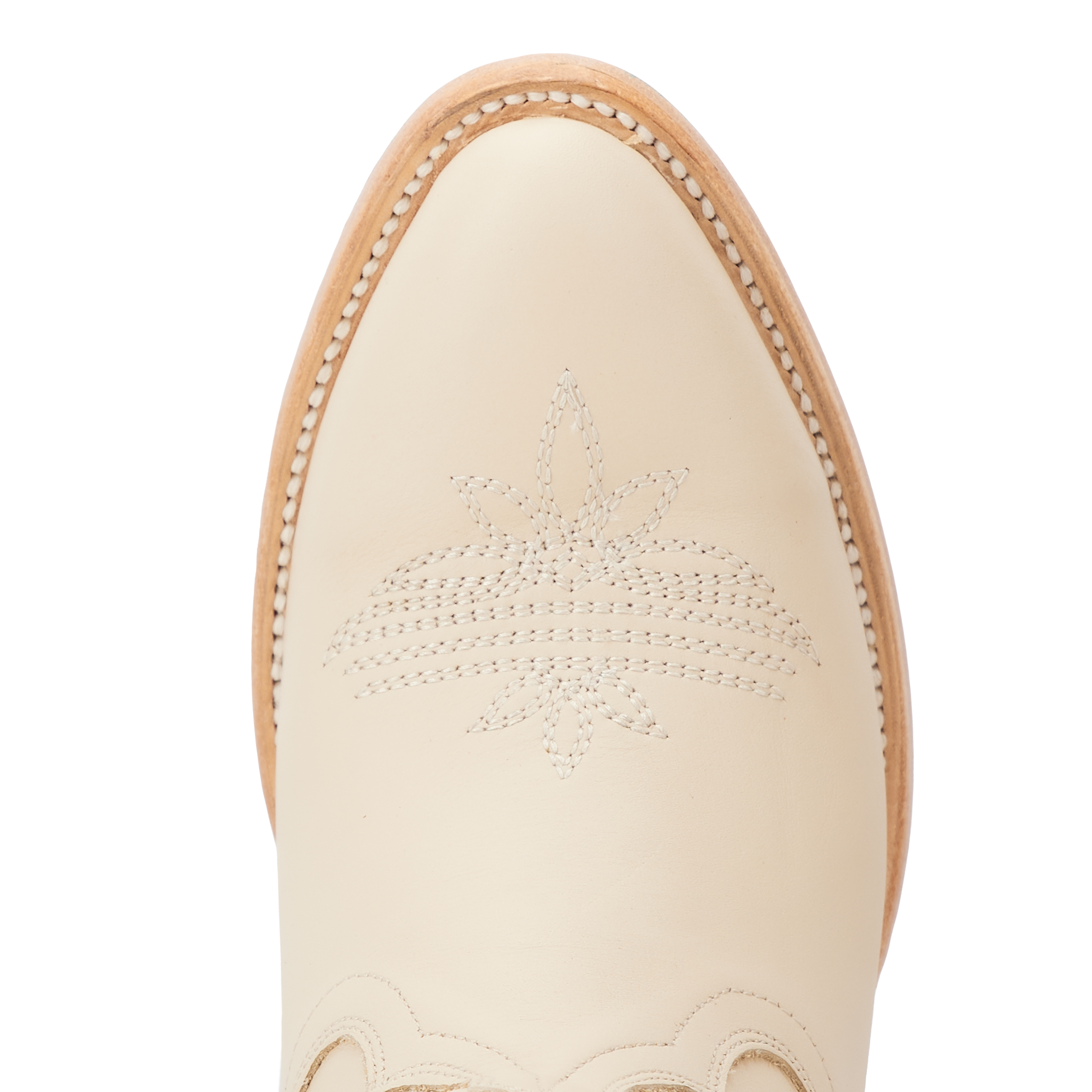 Close-up top view of a cream colored cowboy boot toe with intricate stitched floral and curved line patterns, framed by light-colored welt stitching