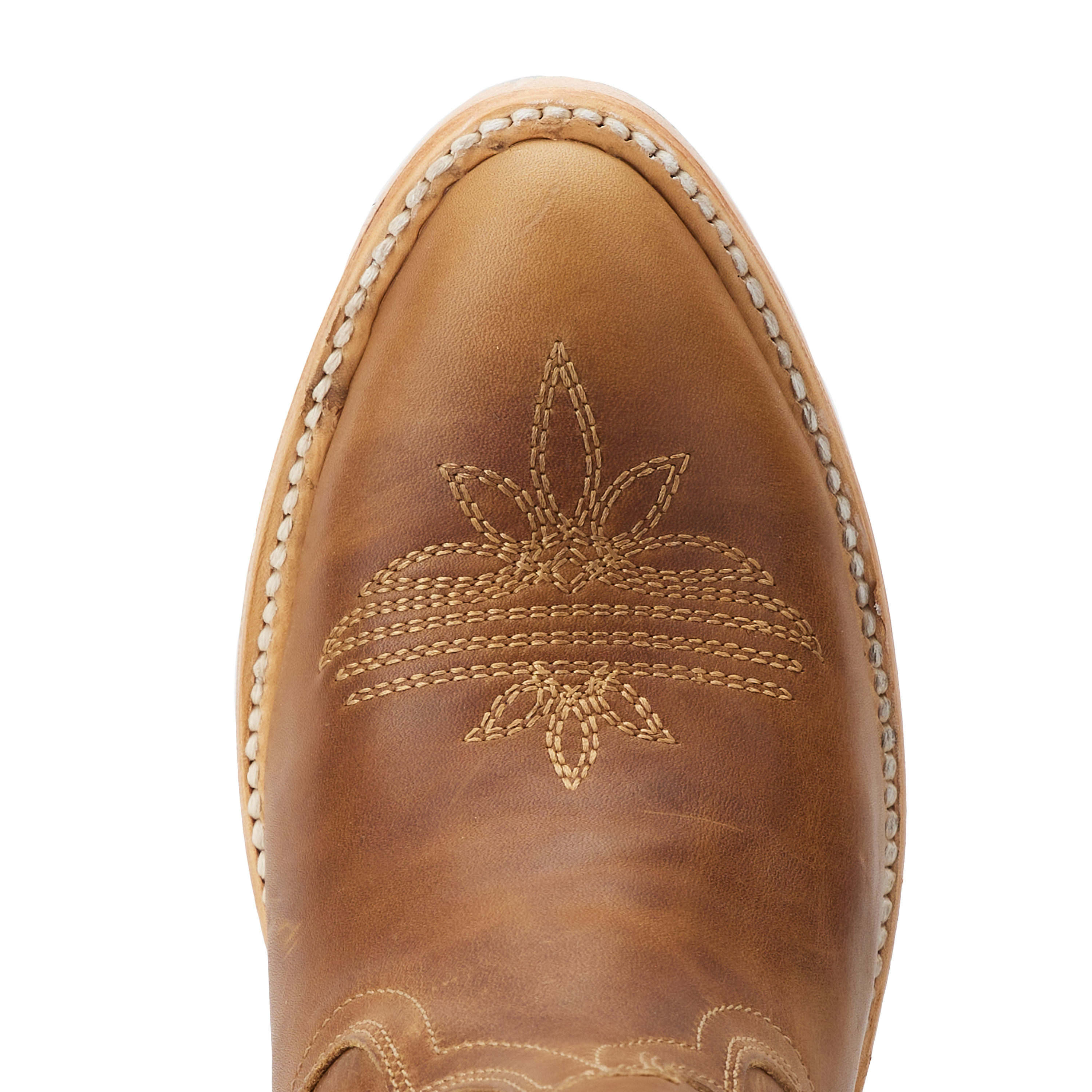 Close-up top view of a brown cowboy boot toe with intricate stitched floral and curved line patterns, framed by light-colored welt stitching